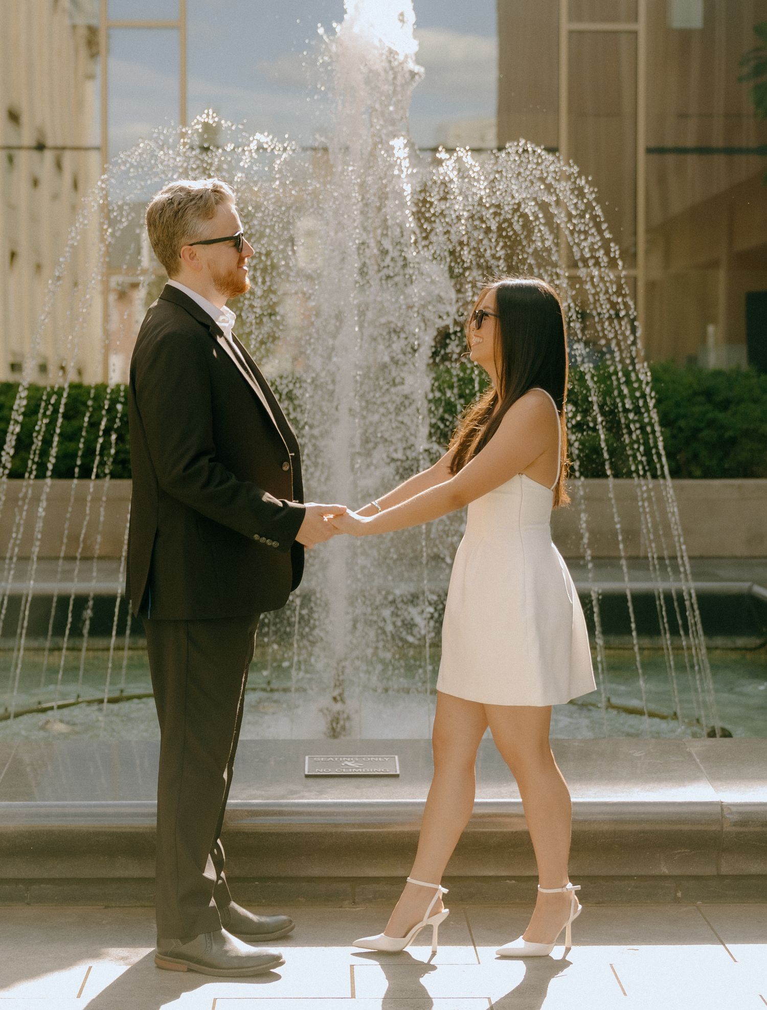 Couple dancing playfully by a water fountain outside a classic building.