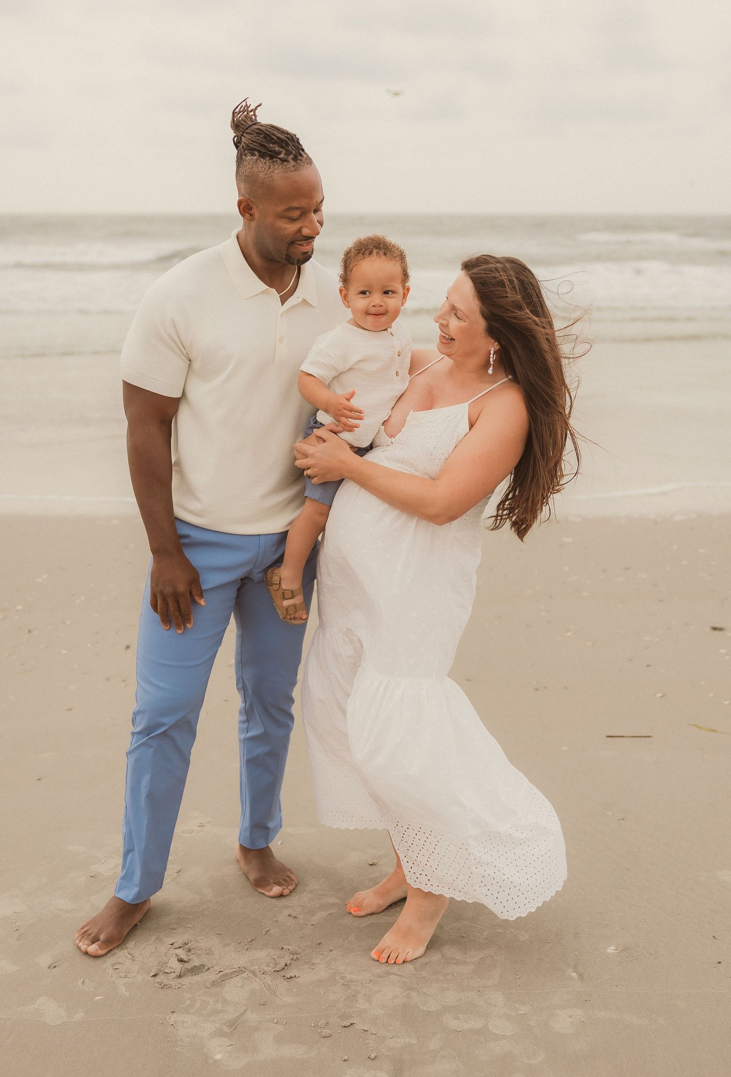 Family playing and laughing together on a sandy beach with ocean waves in the background.