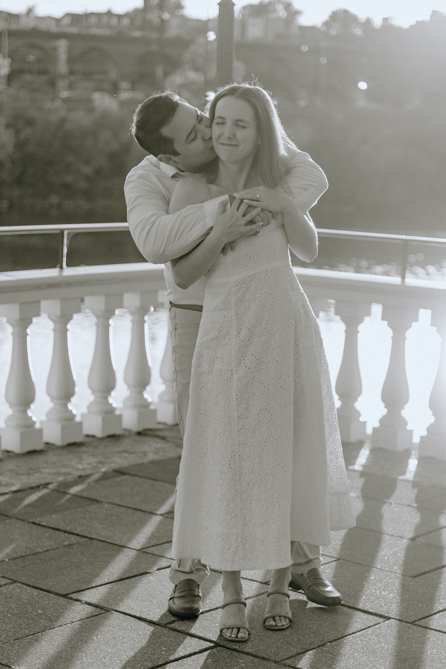Black and white sequence of two children embracing on a balcony with white railings at sunset.