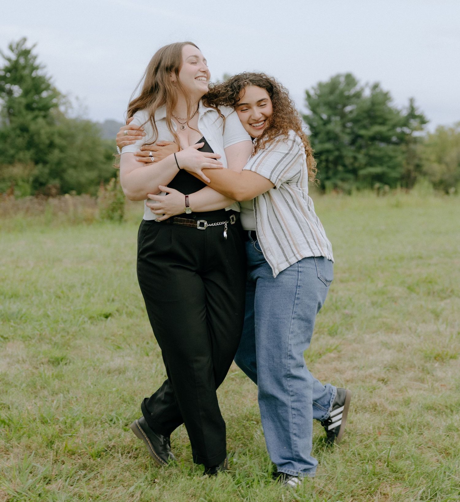 Friends hug and laugh together in a field with trees in the background.