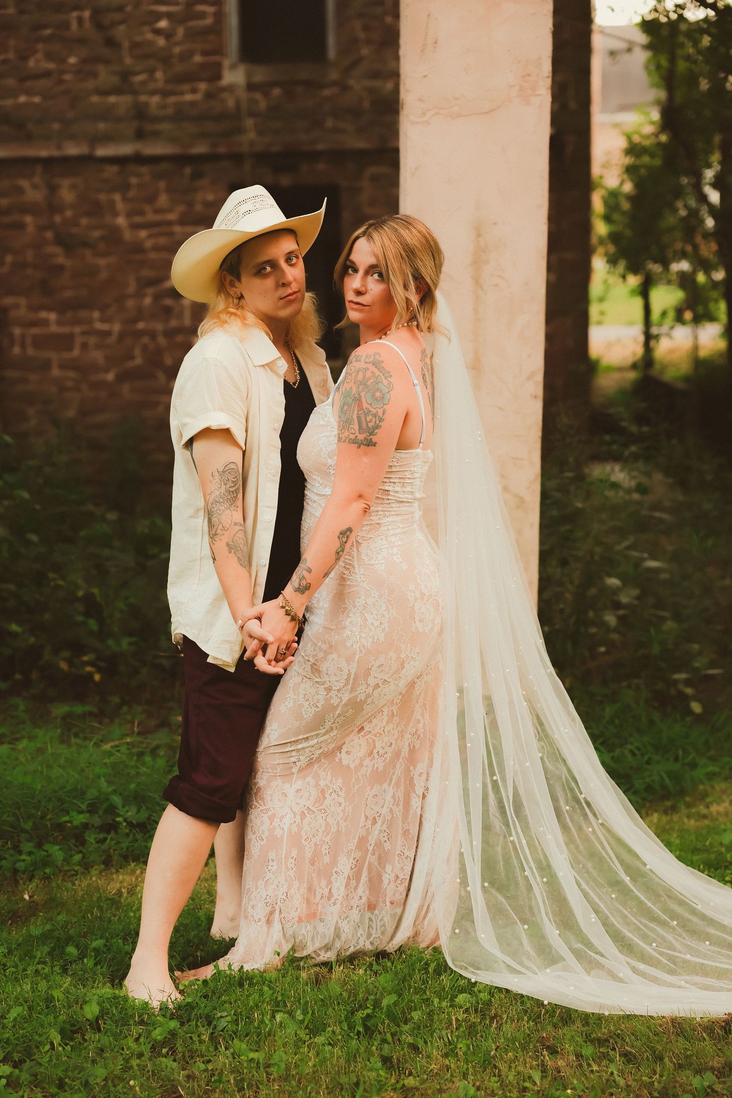 A tender moment between two people in wedding attire against a rustic brick building.