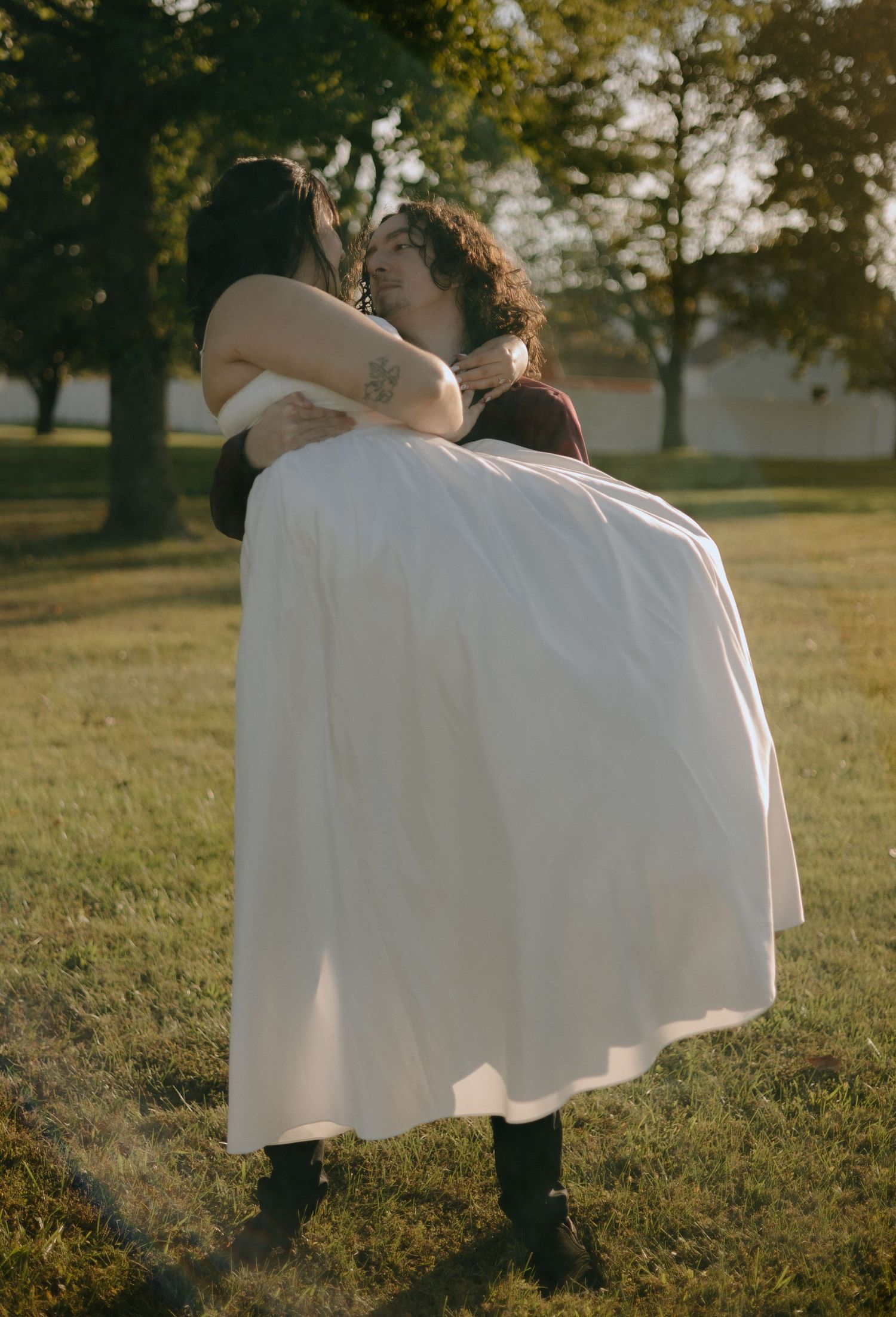 A romantic wedding couple embrace in a sunlit field during golden hour.