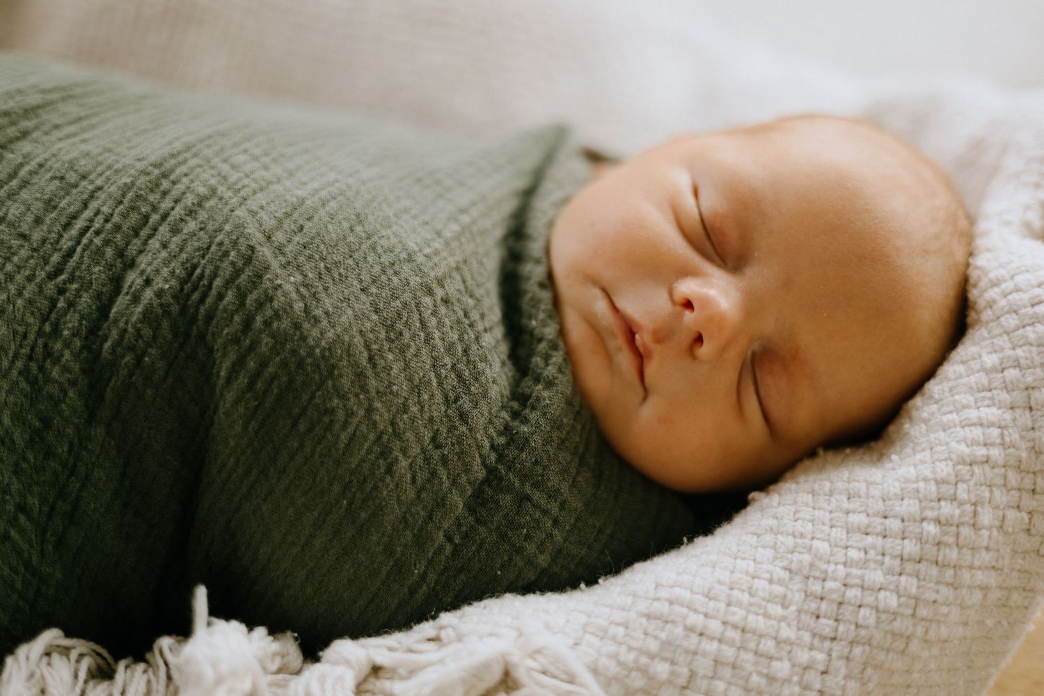 A sleeping infant rests peacefully on a white textured surface in warm lighting.