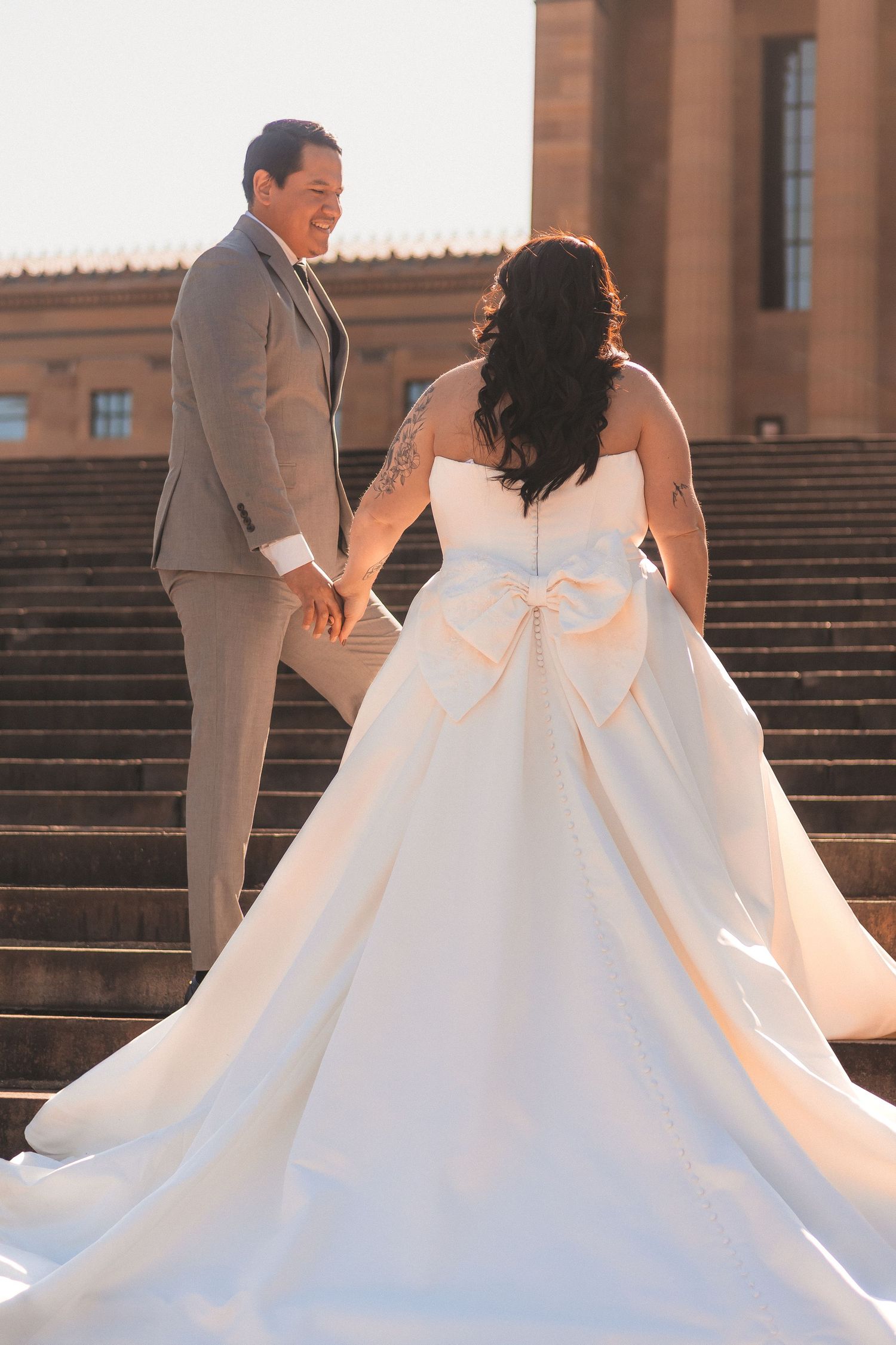 Wedding couple on stone steps with bride's dramatic white ball gown featuring large bow detail.