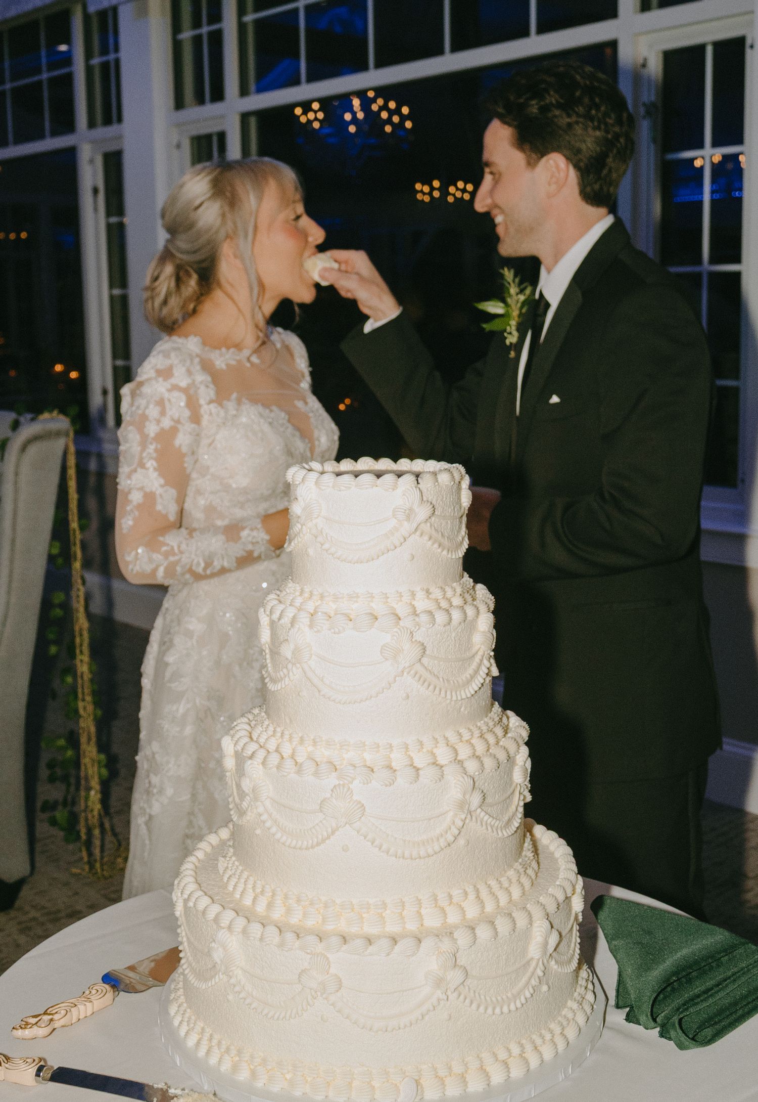A traditional white tiered wedding cake with delicate piped details and pearl decorations displayed at a reception.