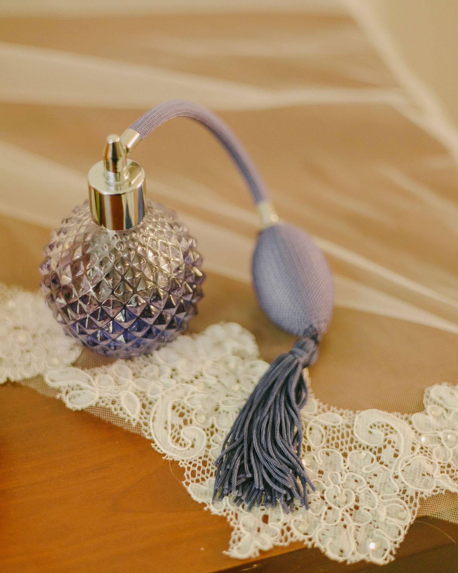 Vintage perfume bottle with gray tassel sits elegantly on delicate white lace doily against wooden surface.