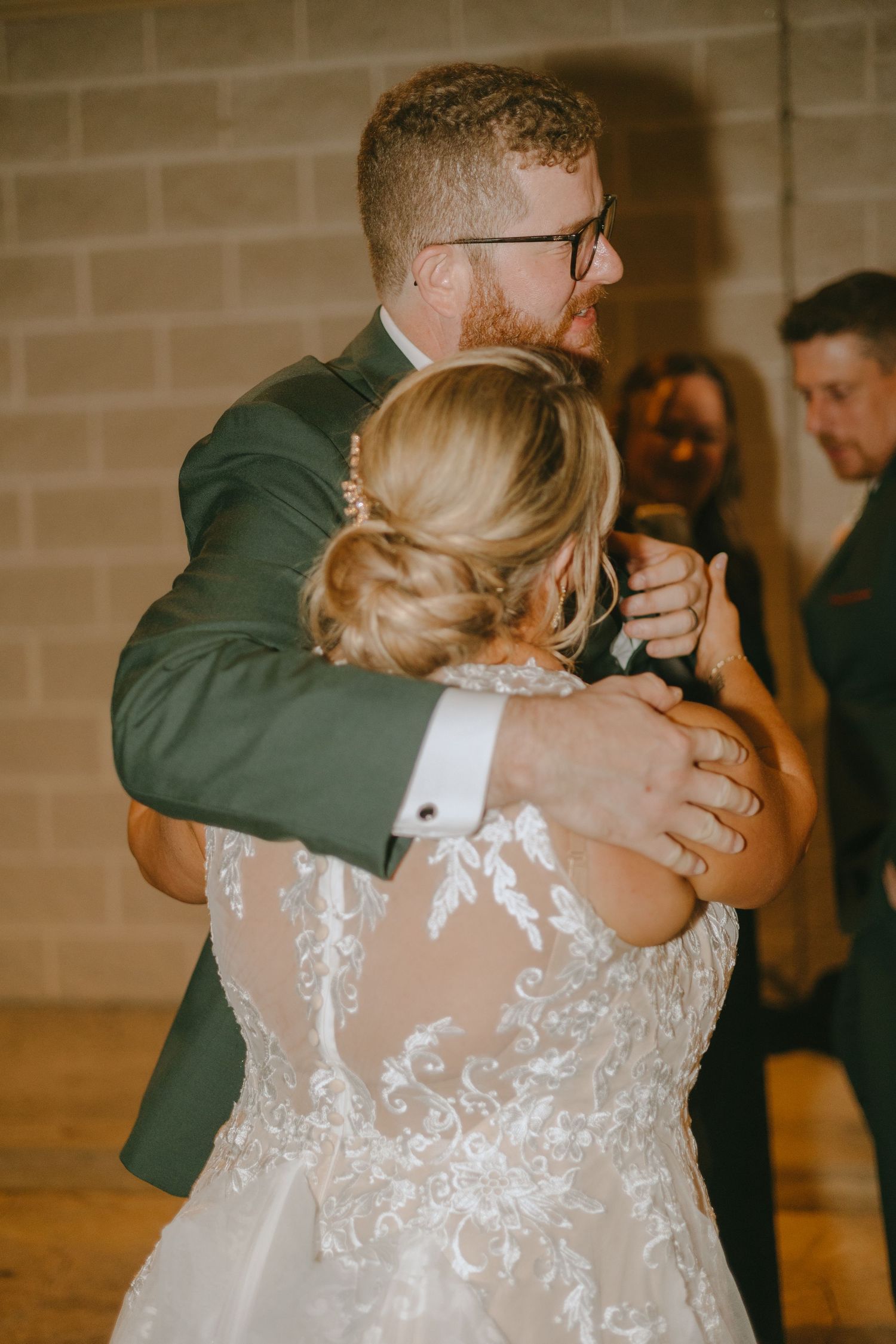 A tender embrace during a wedding dance shows the detailed lace back of a white bridal gown.