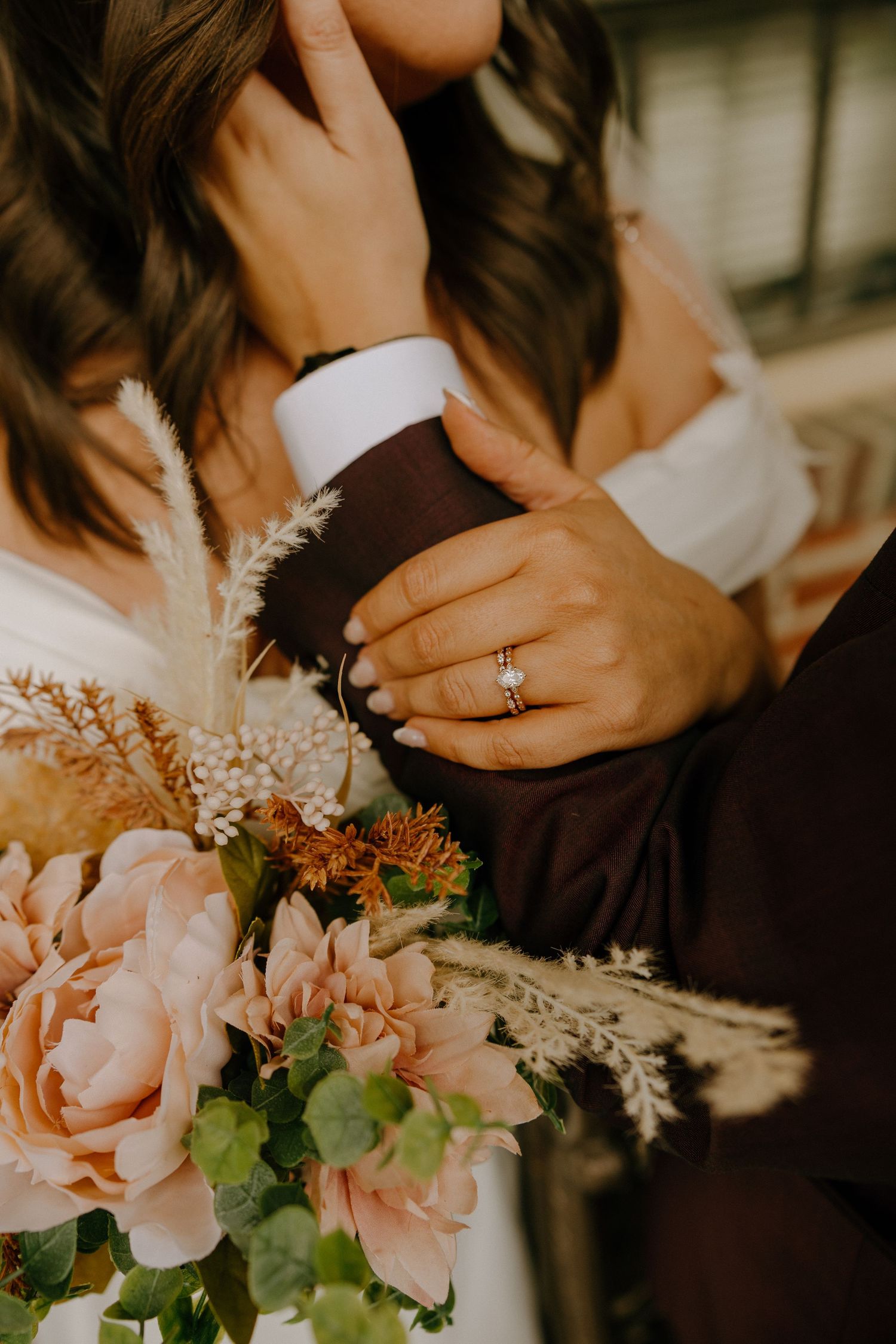Close-up shot of an engagement ring with pink flowers and dried botanicals in the foreground.