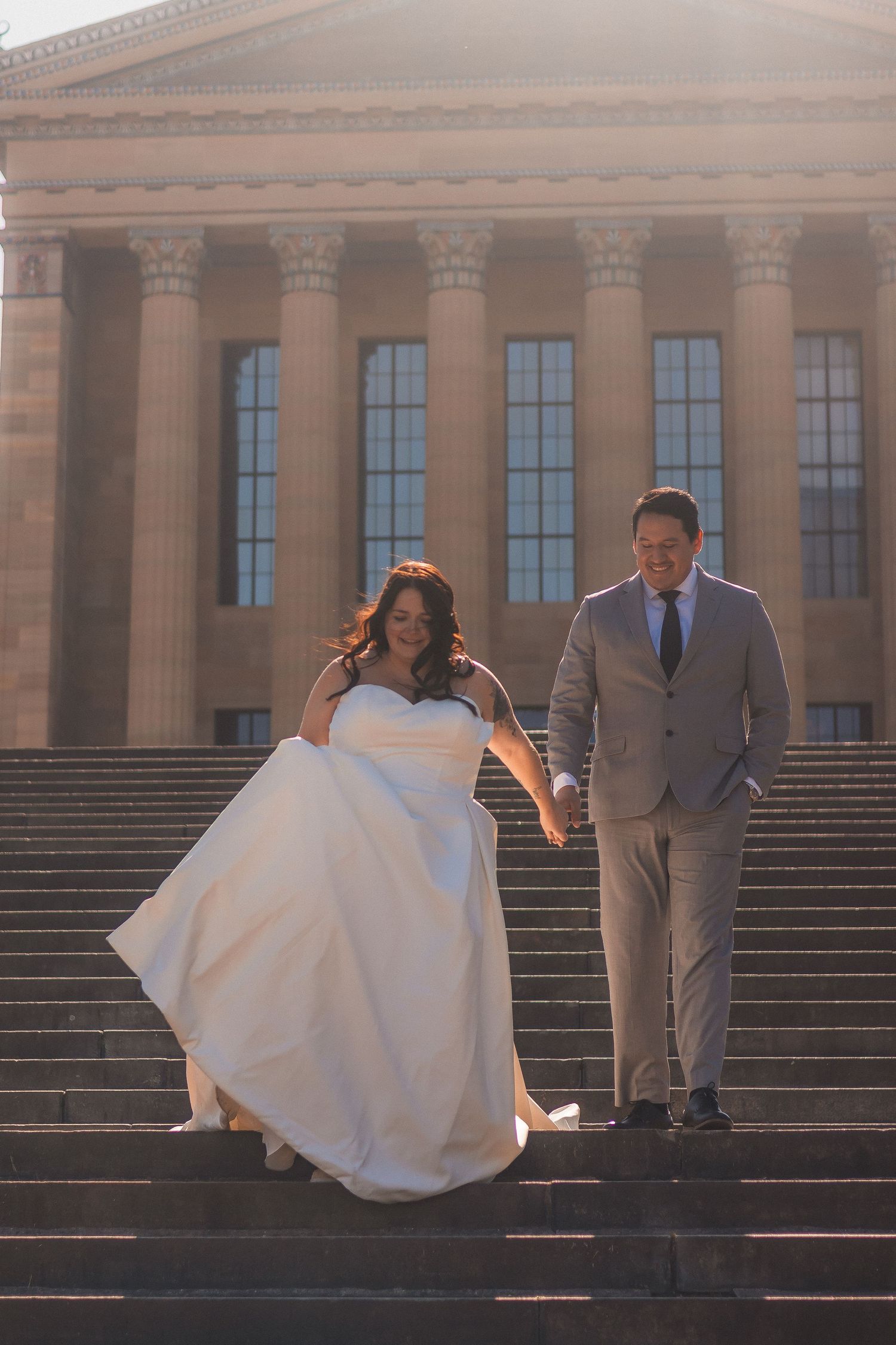 Couple descending grand stone steps at sunset with flowing white wedding dress.