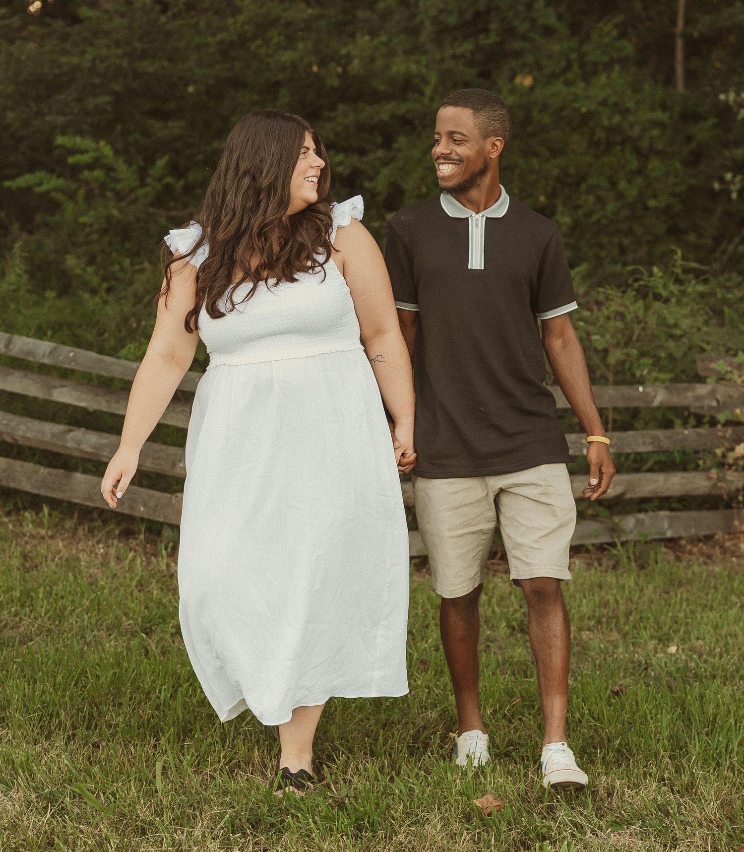 A couple walking hand in hand through a grassy field on a summer day.