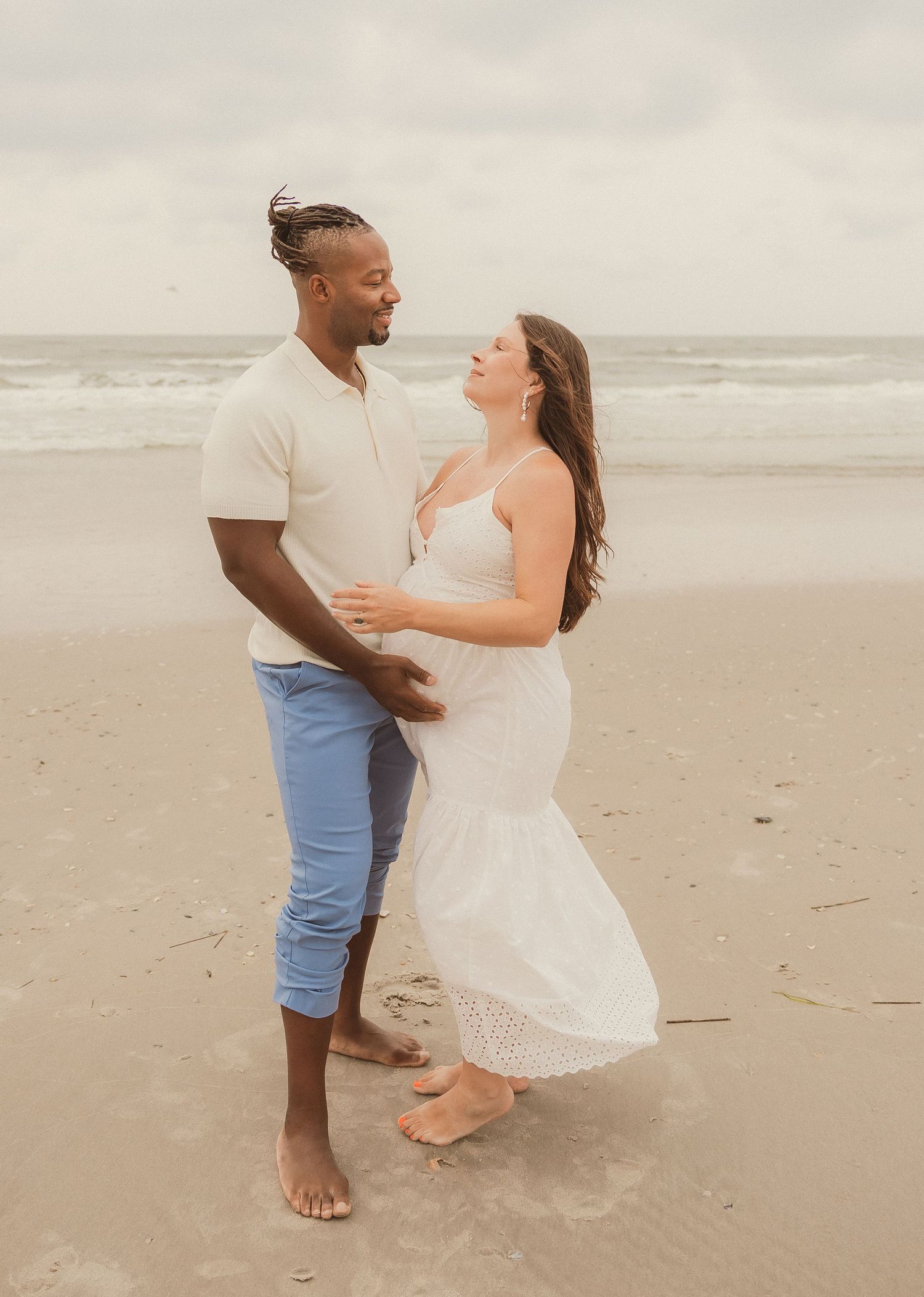 Romantic couple dancing together barefoot on a cloudy beach.