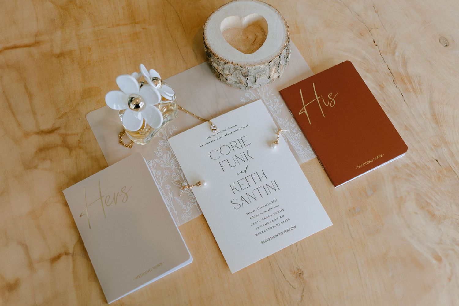 Wedding stationery set with invitation cards, leather notebooks and decorative heart candle holder on beige surface.