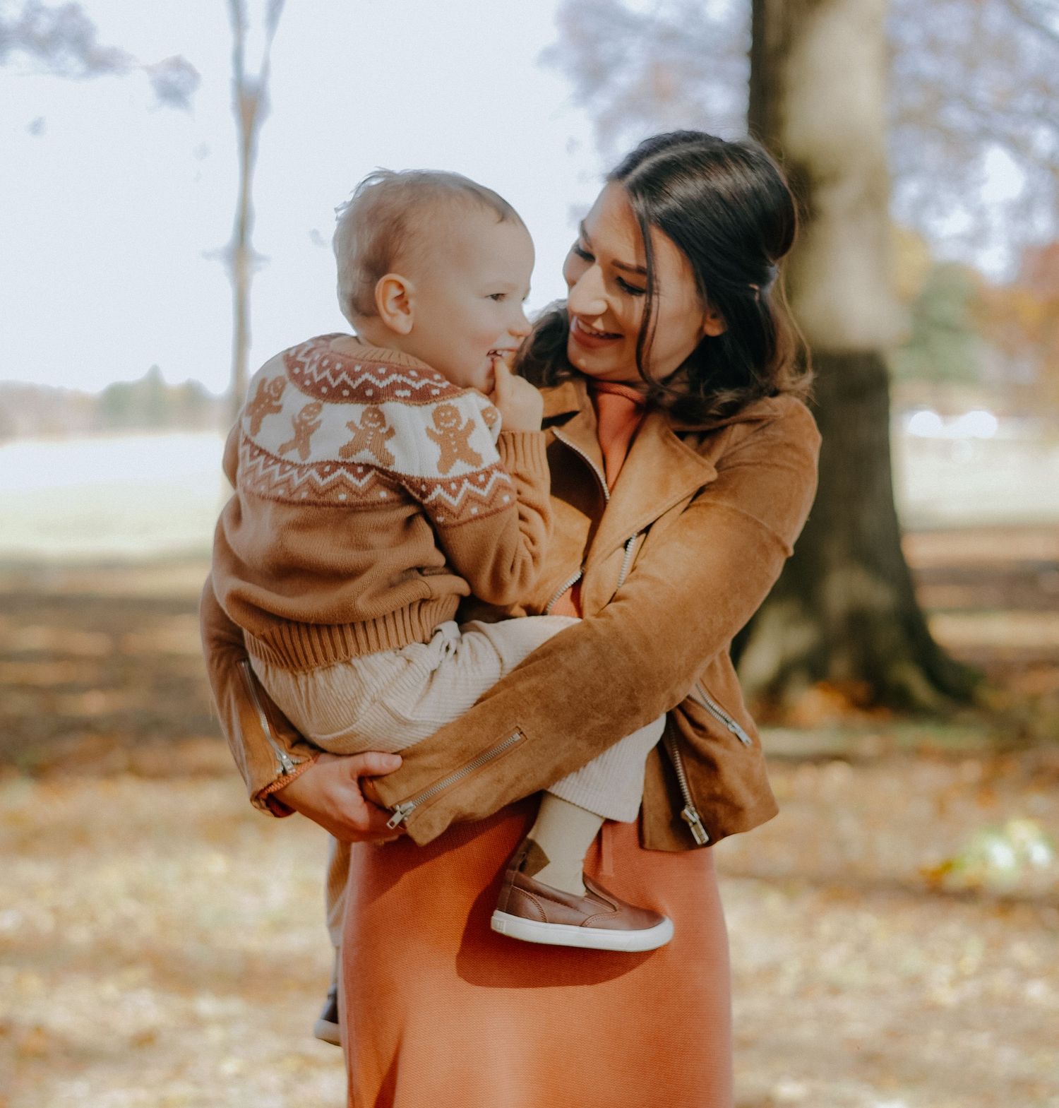 Parent and child share tender moments outdoors in autumn setting with warm lighting and fall foliage.