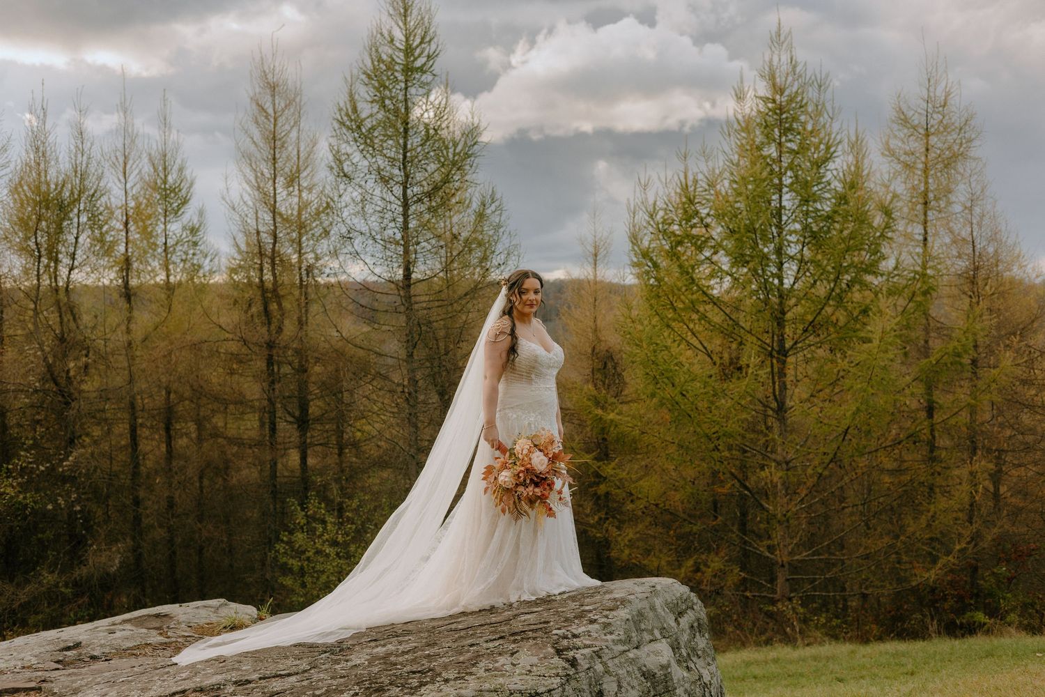 Dramatic wedding portrait with evergreen trees and moody cloudy sky in background.