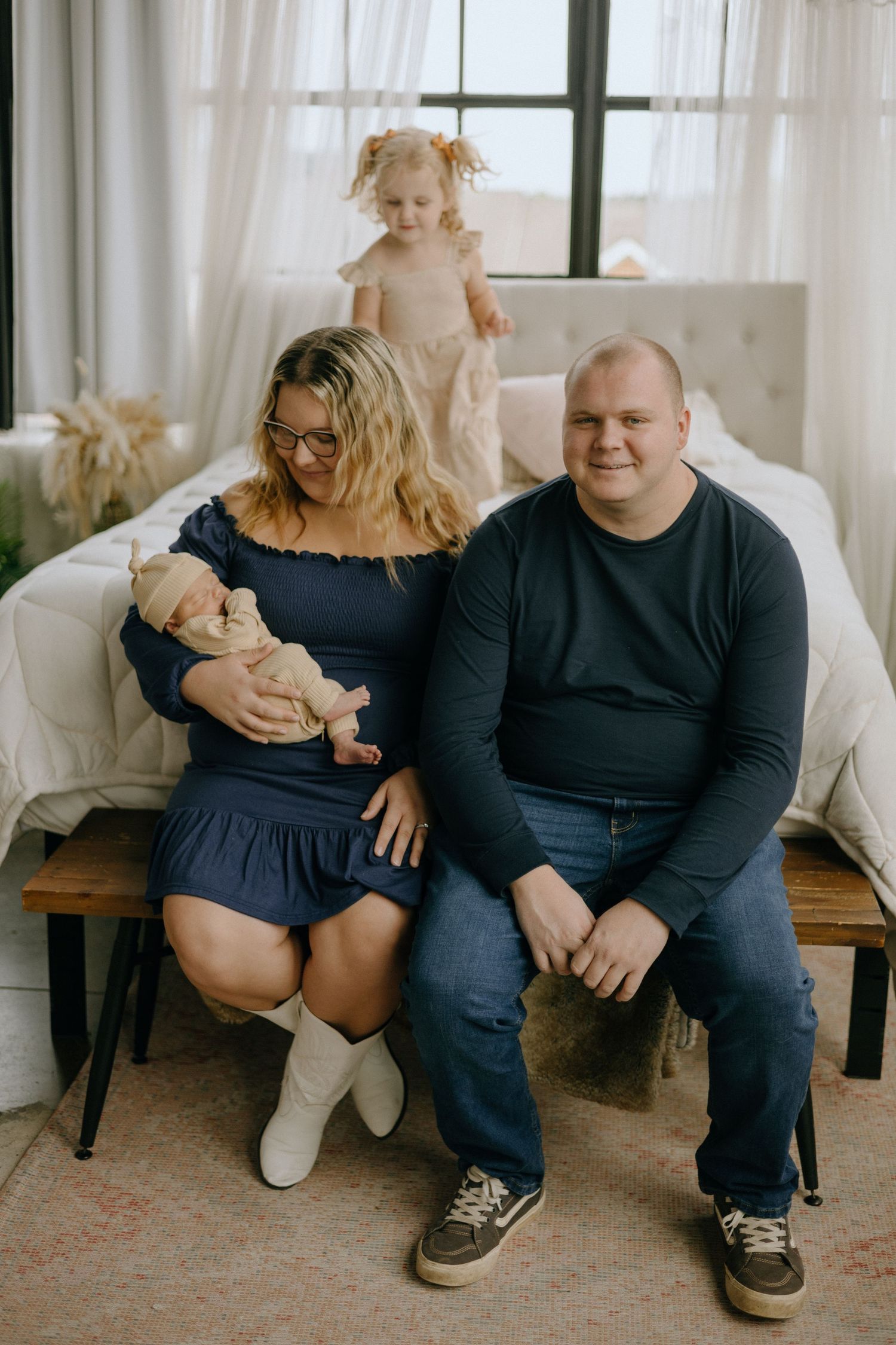 A family sits together on a white couch in a bright room with sheer curtains.
