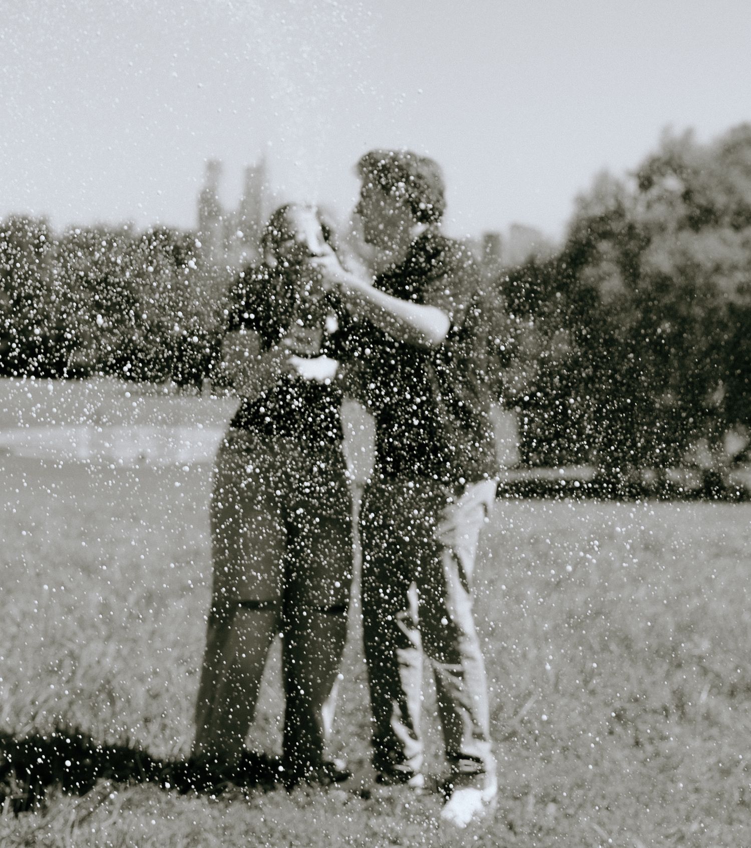 Black and white photo of two people celebrating with champagne spray in an open field.