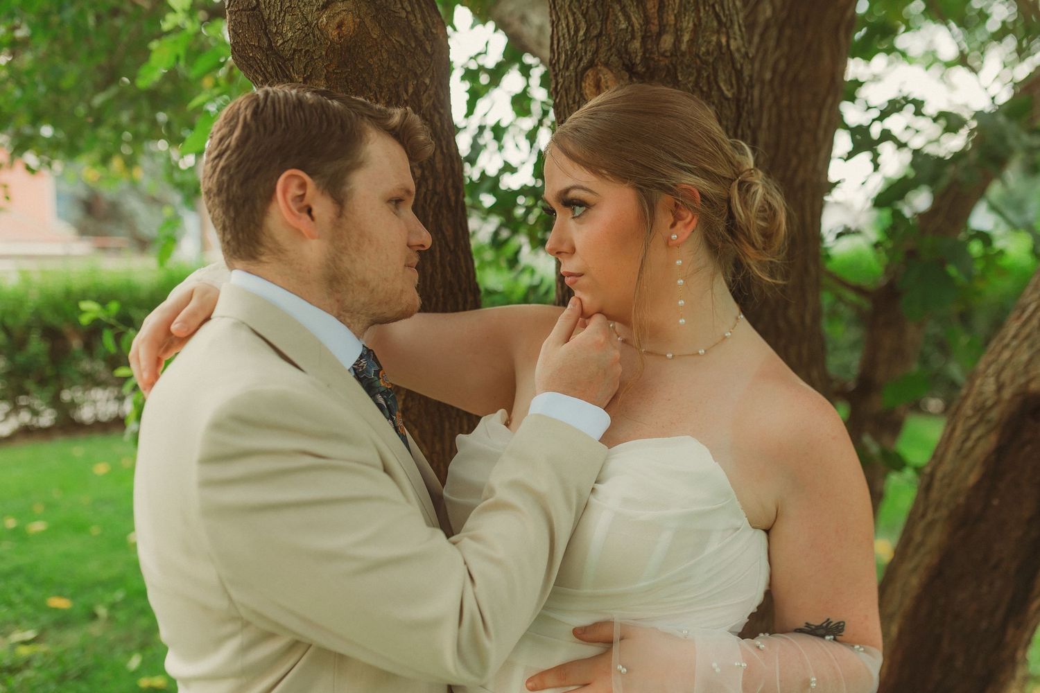 Wedding couple in intimate pose against tree in garden setting.