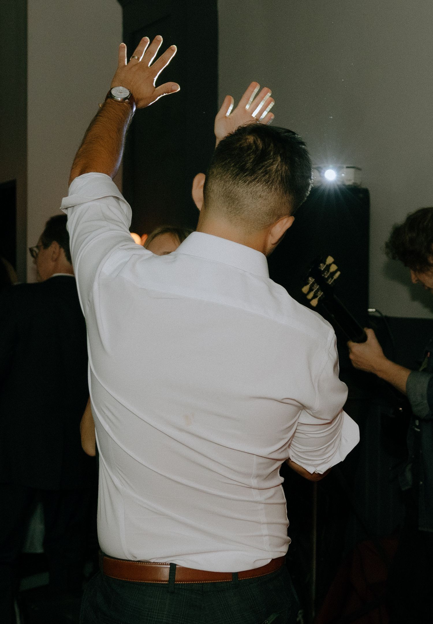 Silhouettes of people dancing and raising their hands in a dark reception venue.