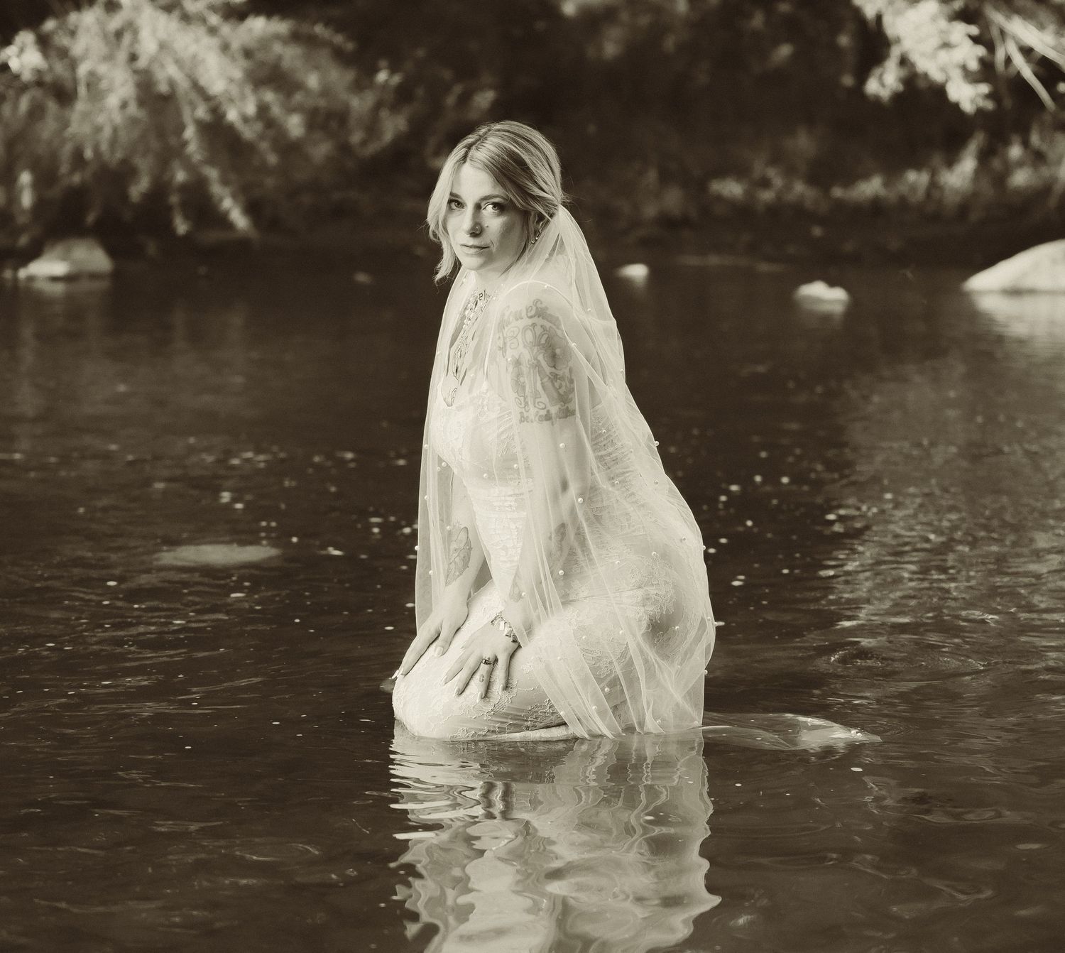 A monochrome photograph of a person in a wedding dress standing in reflective water.