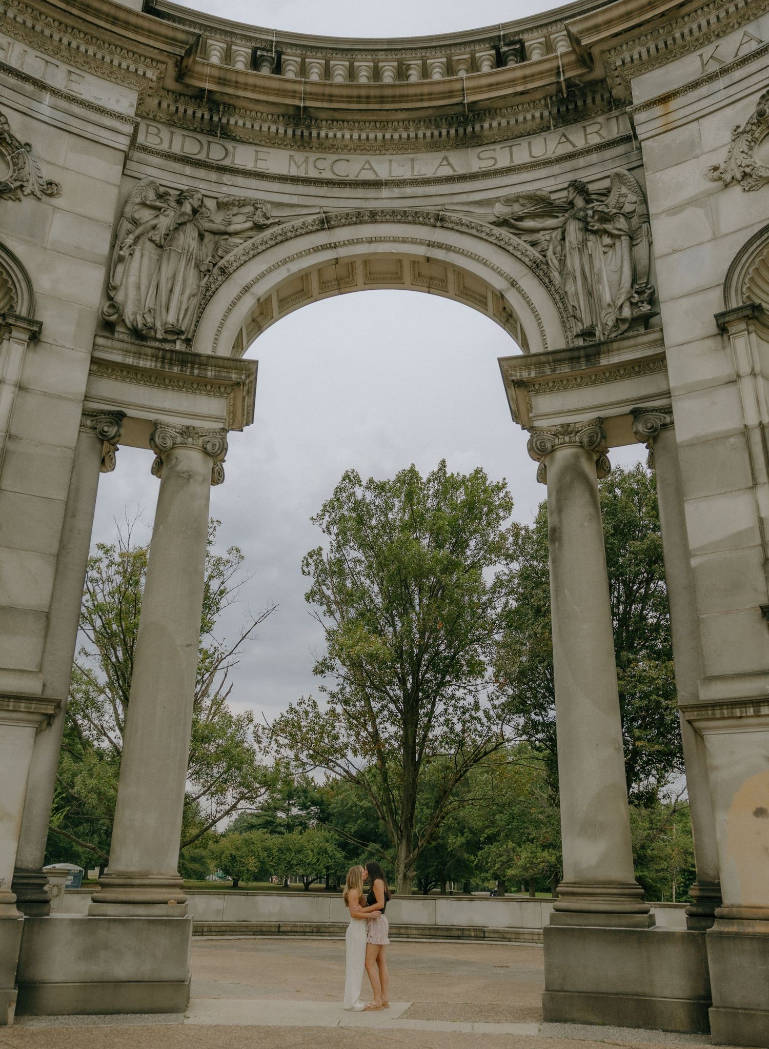 An elegant stone archway with classical columns frames a garden view in a serene outdoor setting.
