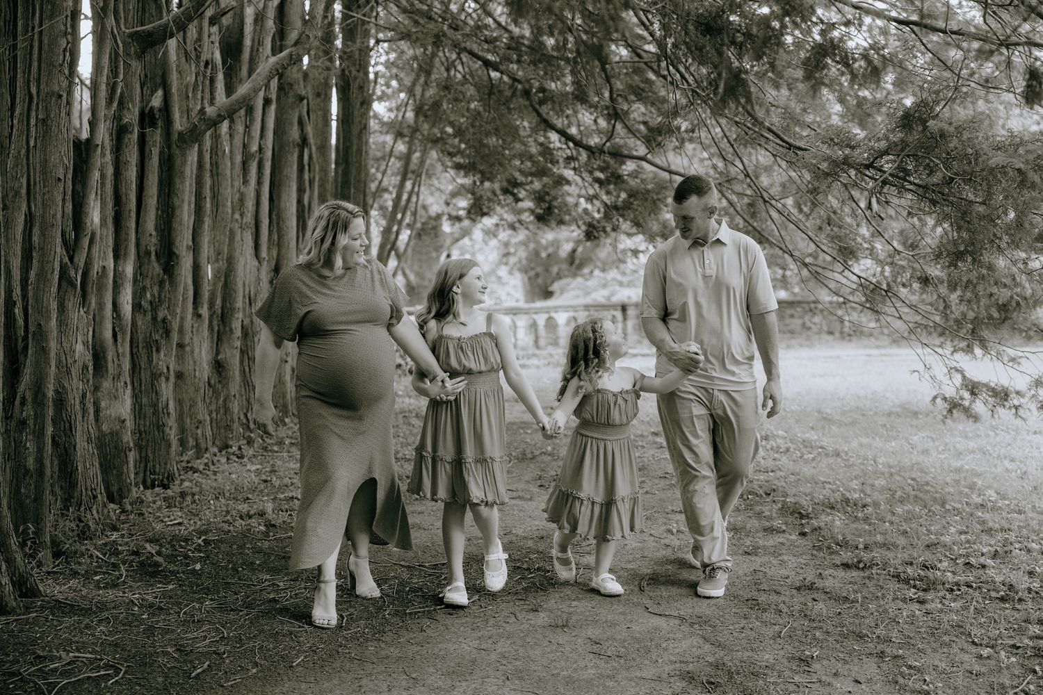 Black and white photo of family walking along wooded path in matching outfits.