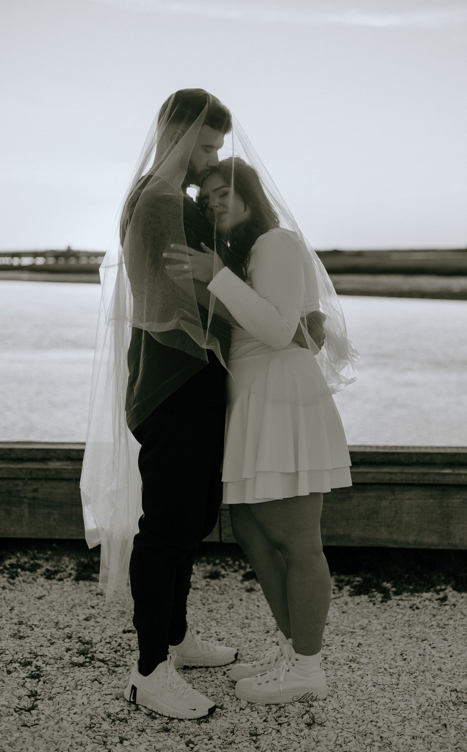Black and white romantic scene by the waterfront with a couple in contrasting outfits.