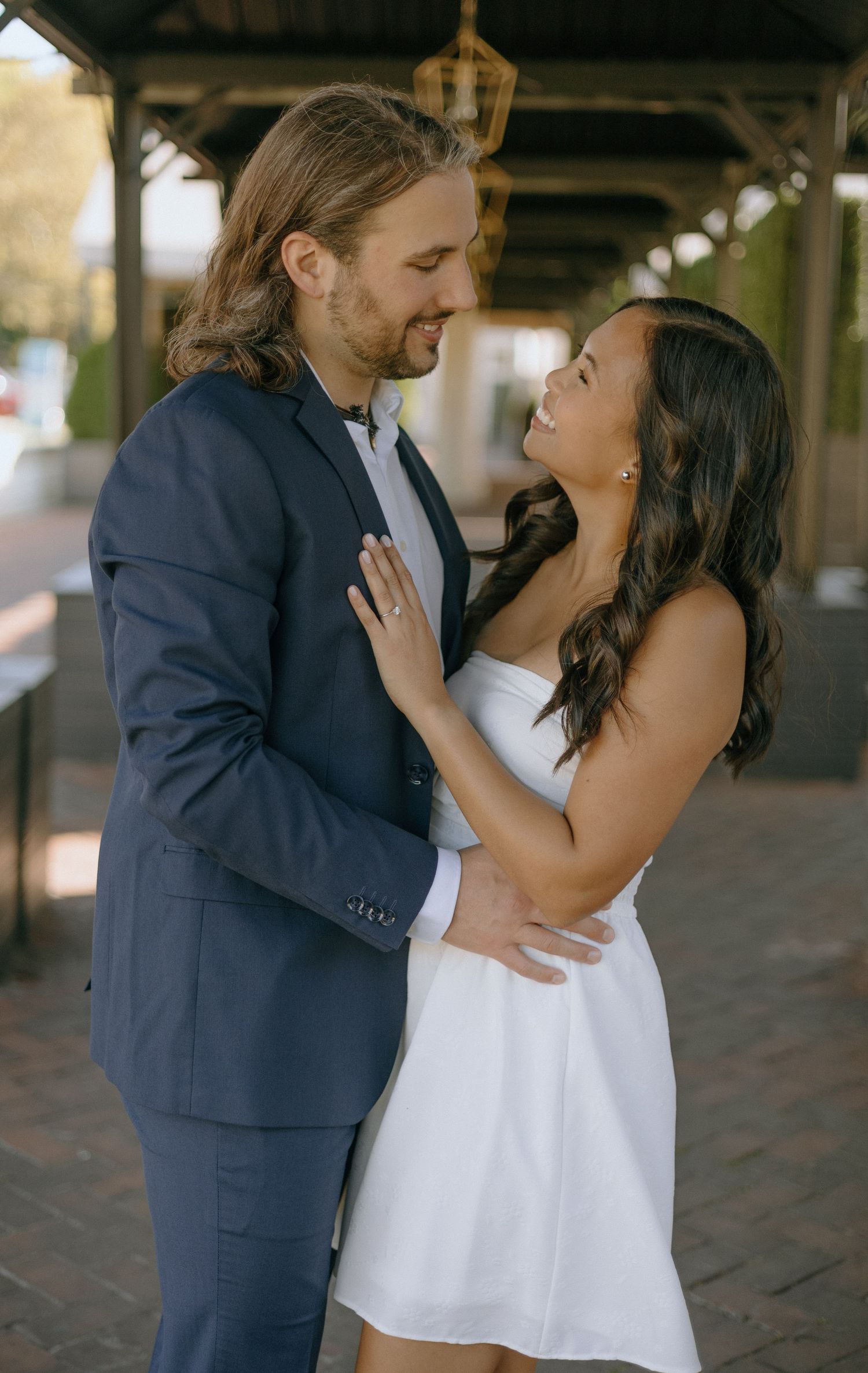 A romantic couple in formal attire share tender moments under an architectural structure.