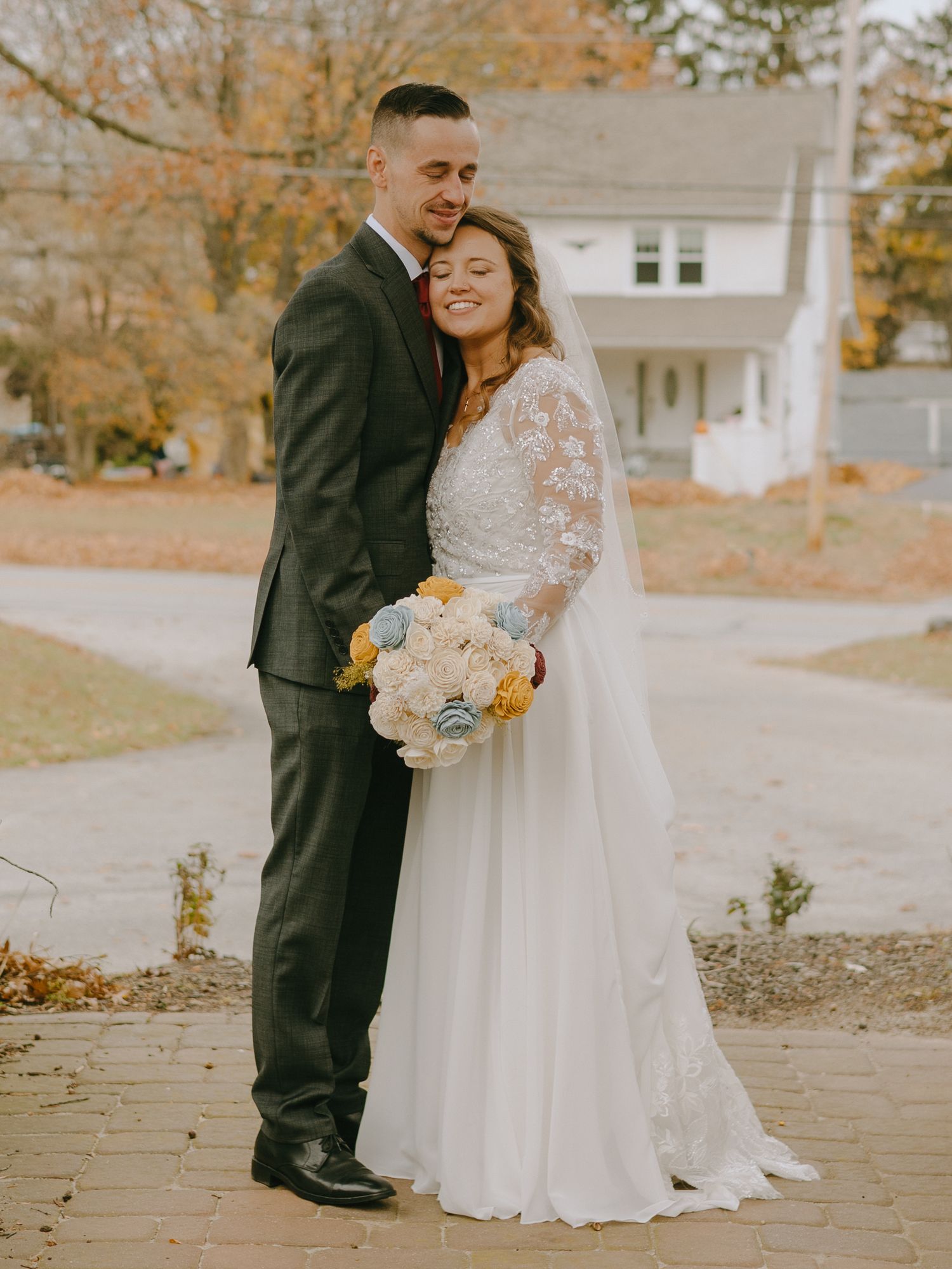A couple in wedding attire stands together on fallen autumn leaves during their outdoor fall ceremony.