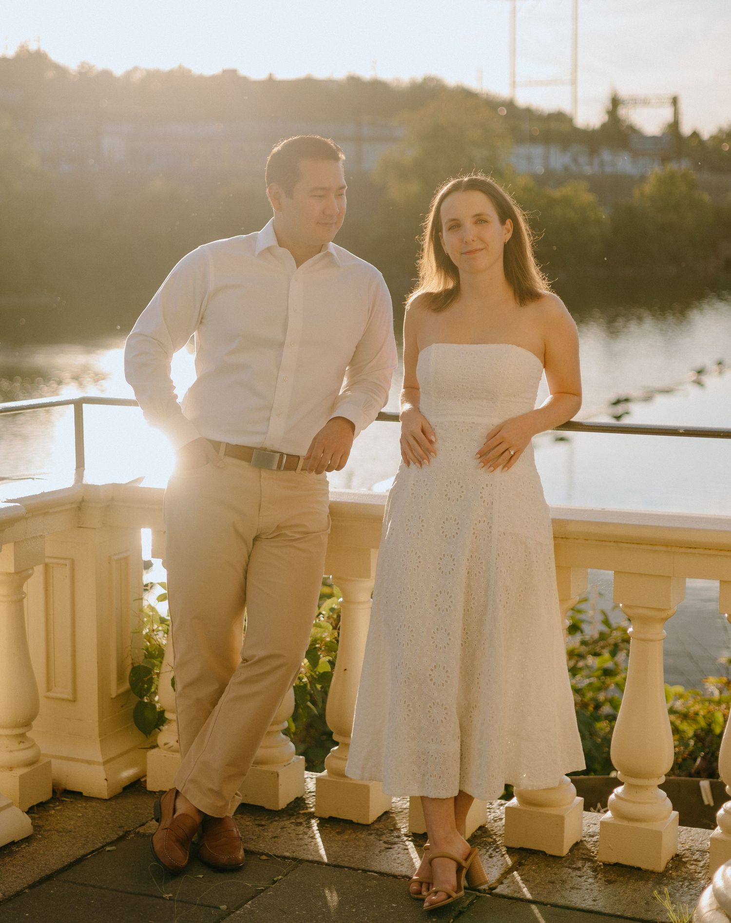 A couple sits together on a stone balustrade during golden hour, creating a romantic silhouette against the sunset.