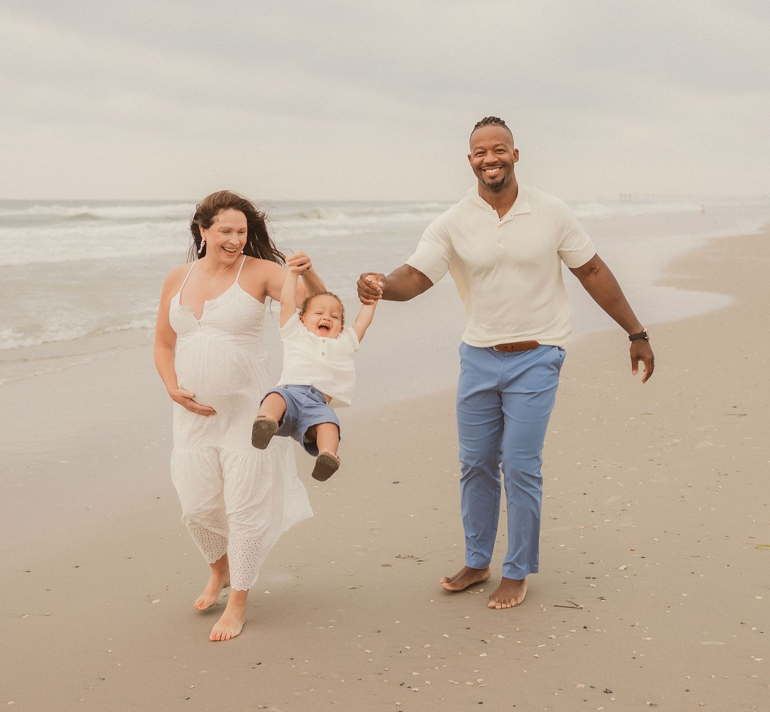 Playful family portrait session on beach with bright sandy background.
