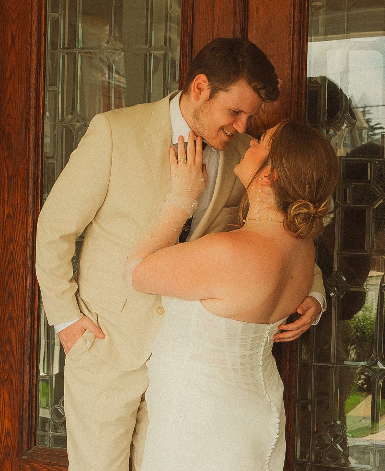 Intimate wedding photo of couple in cream suit and white dress sharing close moment.