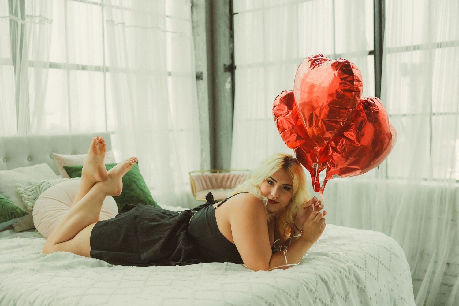 Dreamy boudoir scene with flowing white curtains and red heart balloons as props.