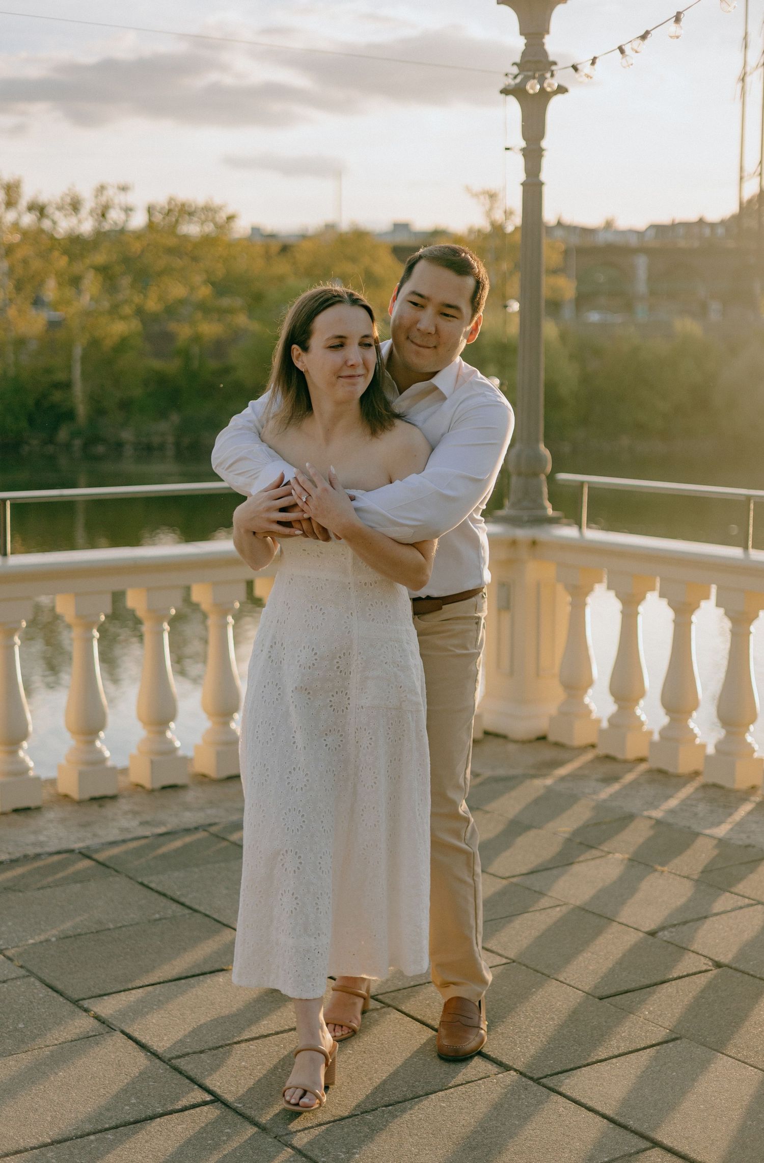 A romantic couple dances together on an elegant balcony with white stone balusters during golden hour.