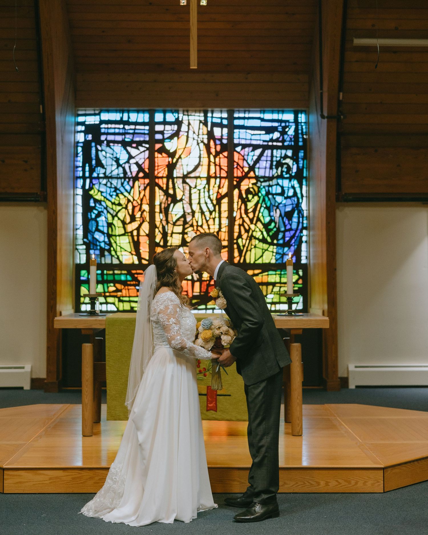 A couple performs a dance move in front of colorful stained glass windows during their wedding ceremony.