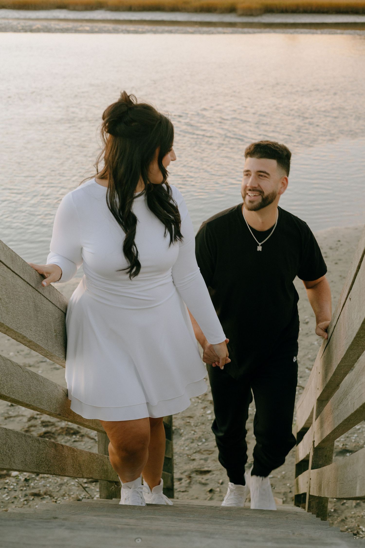 A couple in contrasting black and white outfits walking up concrete steps near a waterfront.