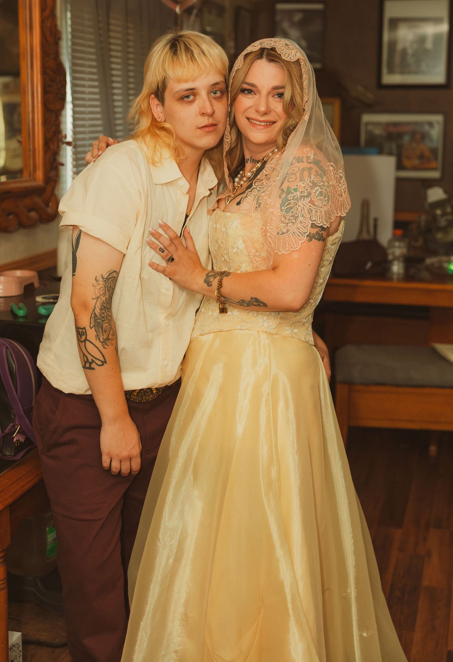A couple embraces while wearing vintage-inspired wedding attire in an indoor setting with wooden details.