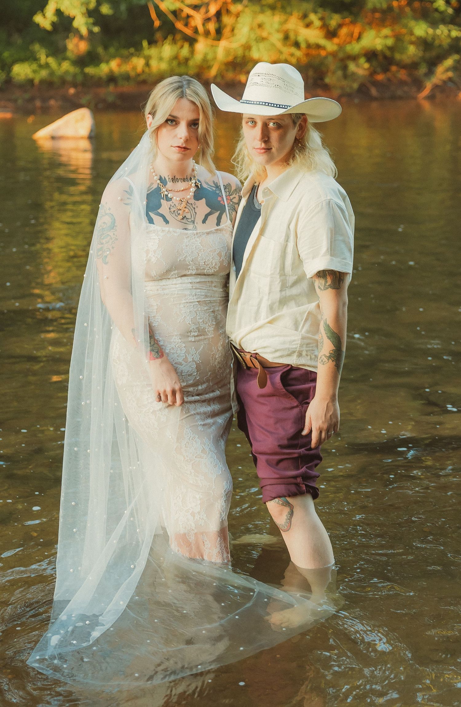 Two people share an intimate moment while standing knee-deep in a sunlit river.