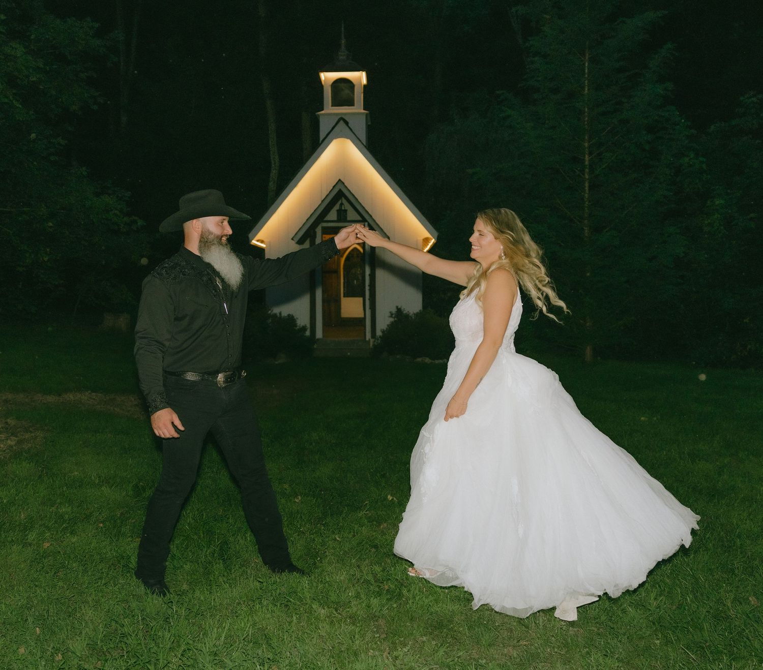 Wedding couple playfully posing outside a garden chapel at night.
