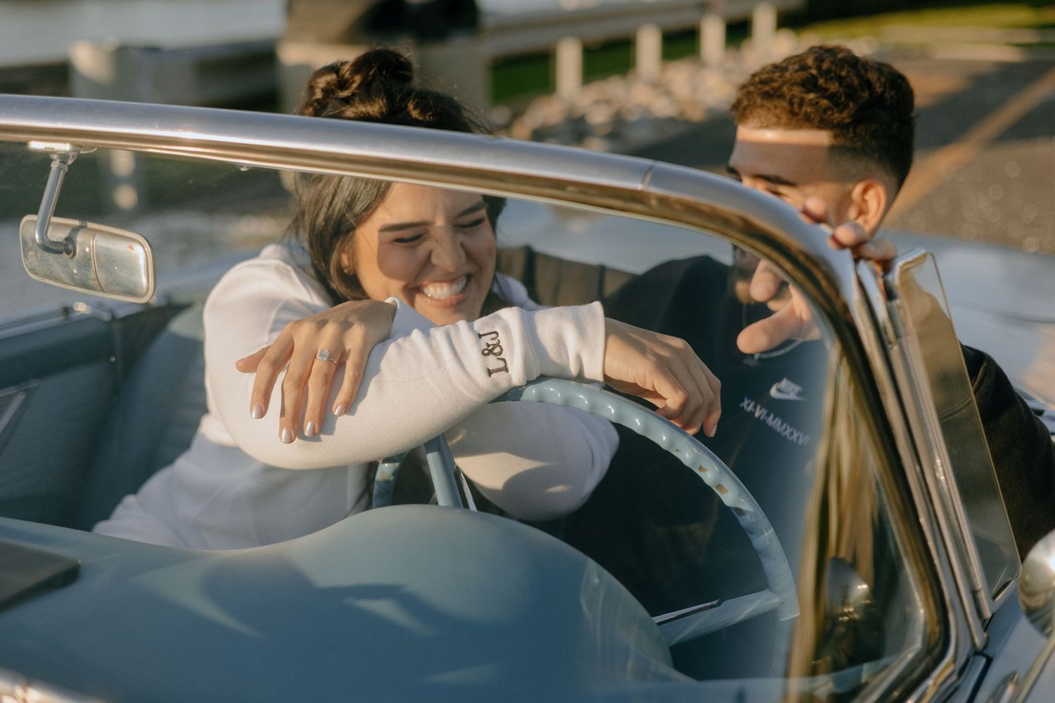 A person helps another person get into the passenger side of a vintage car at sunset.