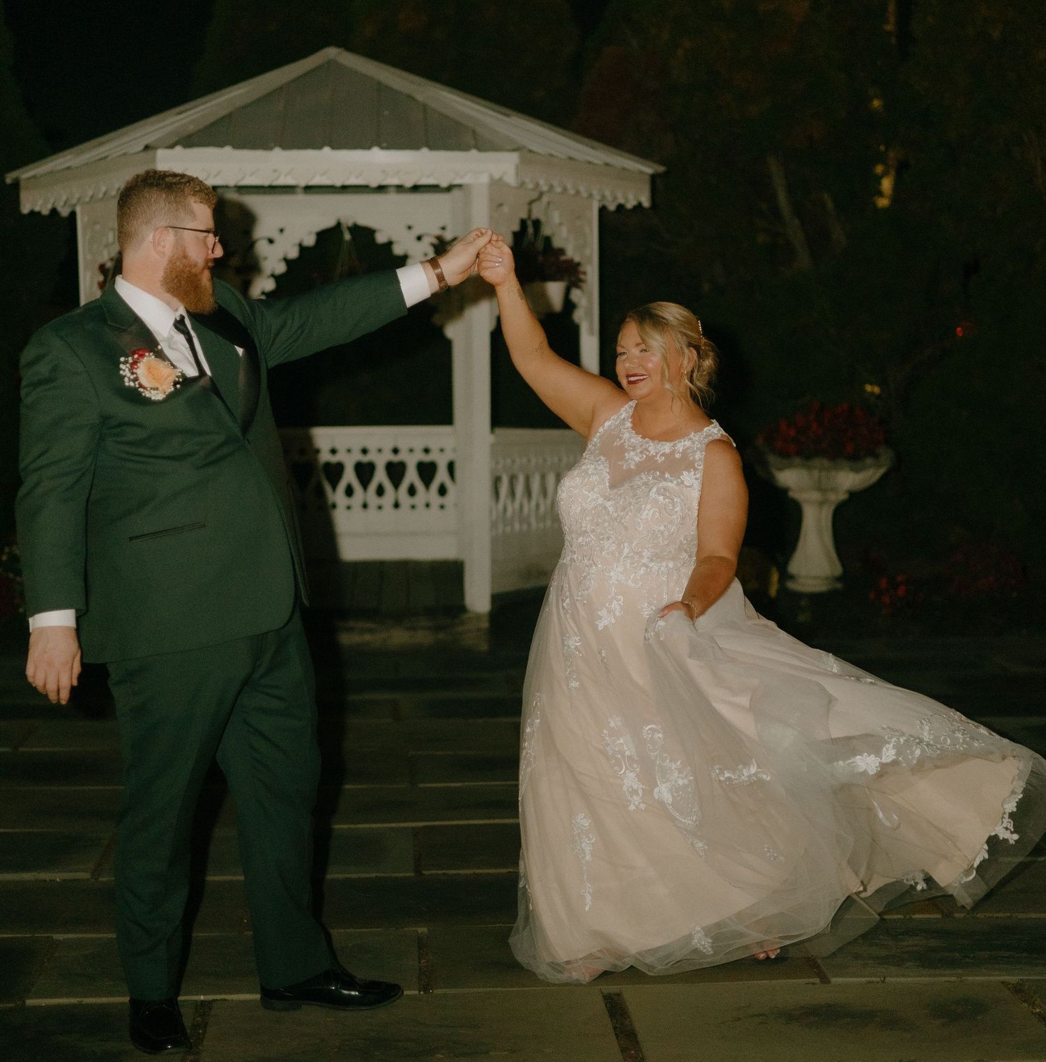 A couple in wedding attire dances and twirls together in a romantic nighttime outdoor setting.