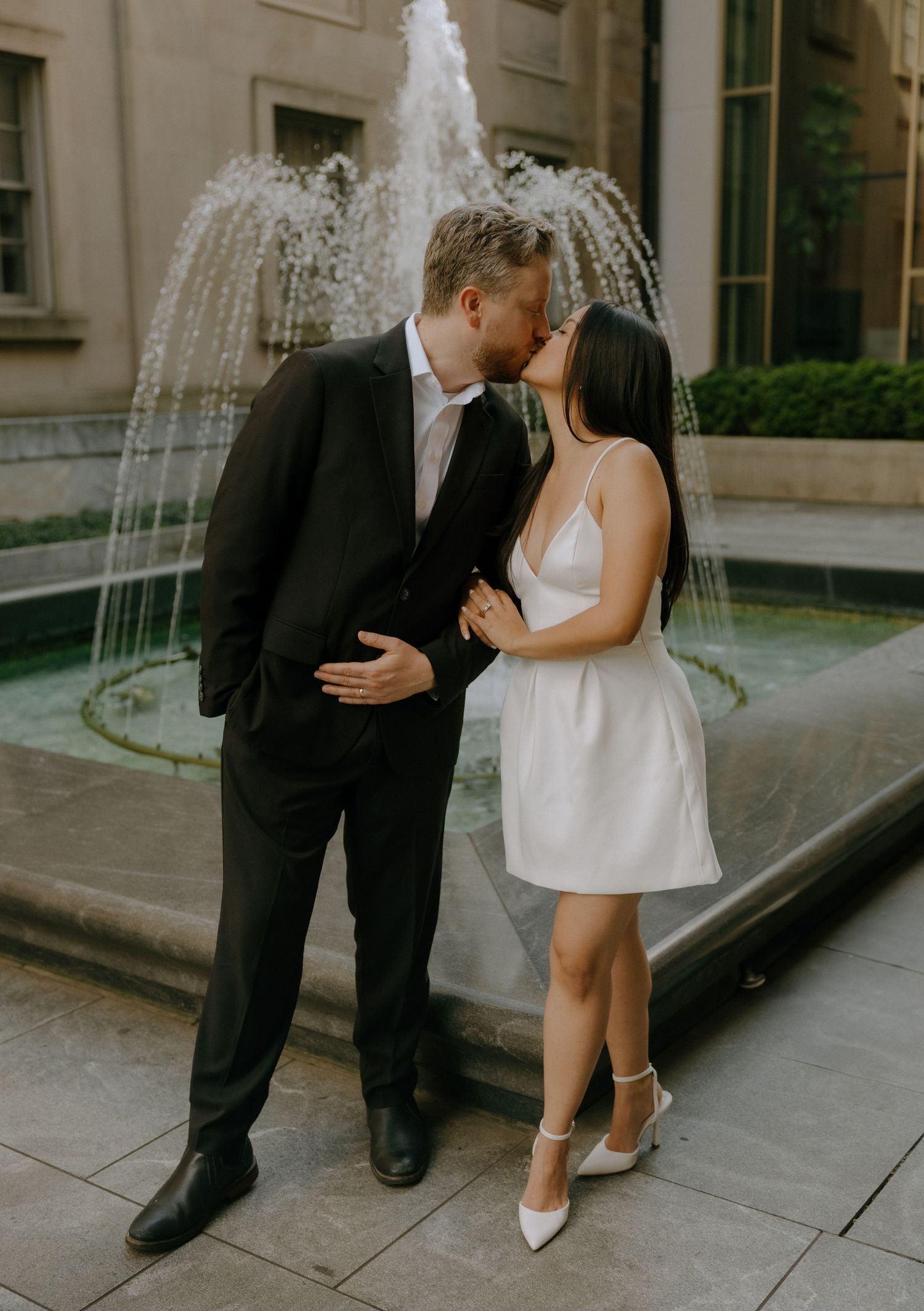 Dancing couple in formal wear performing romantic moves by fountain.