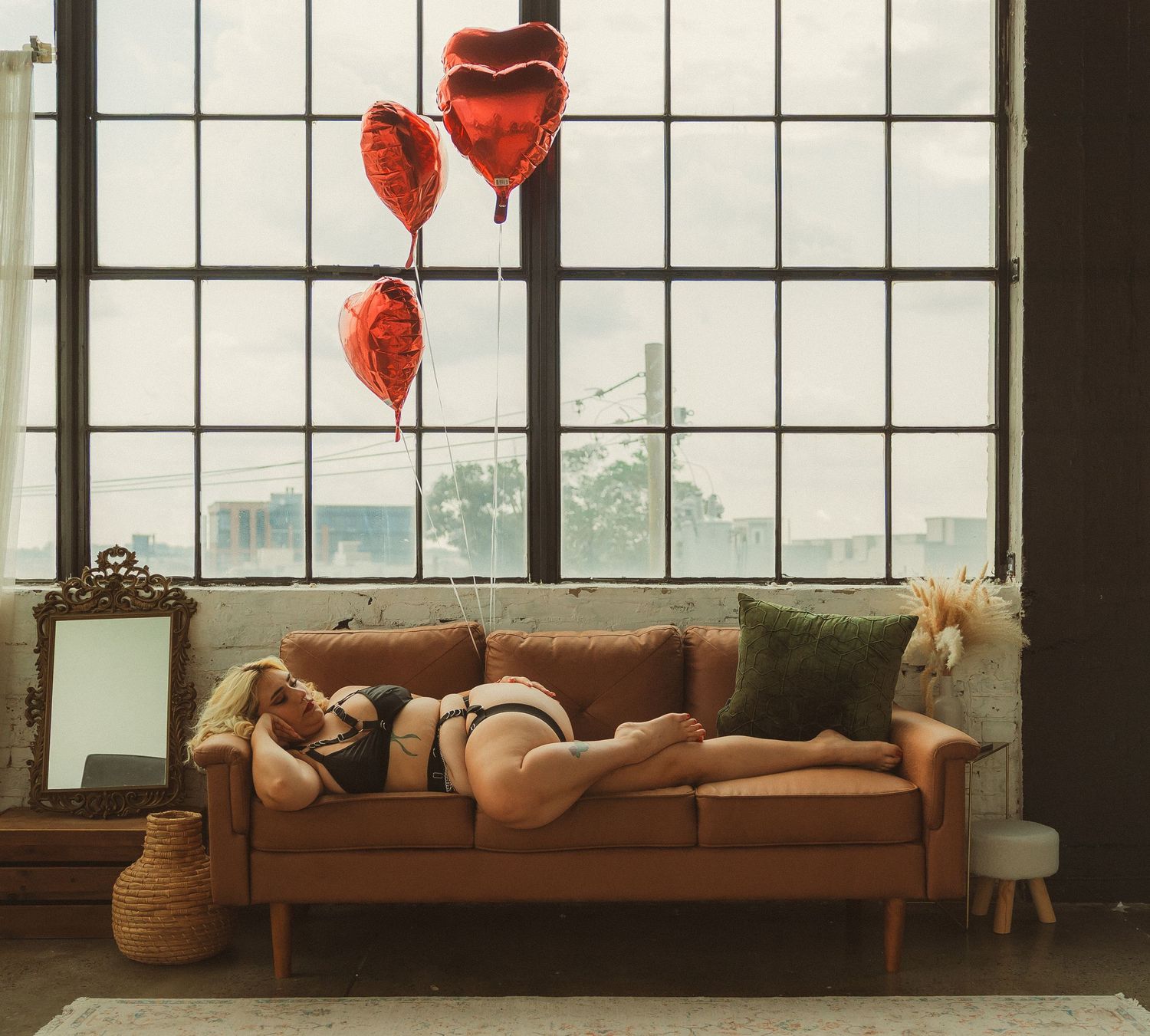 Red heart balloons float near vintage brown leather couch.