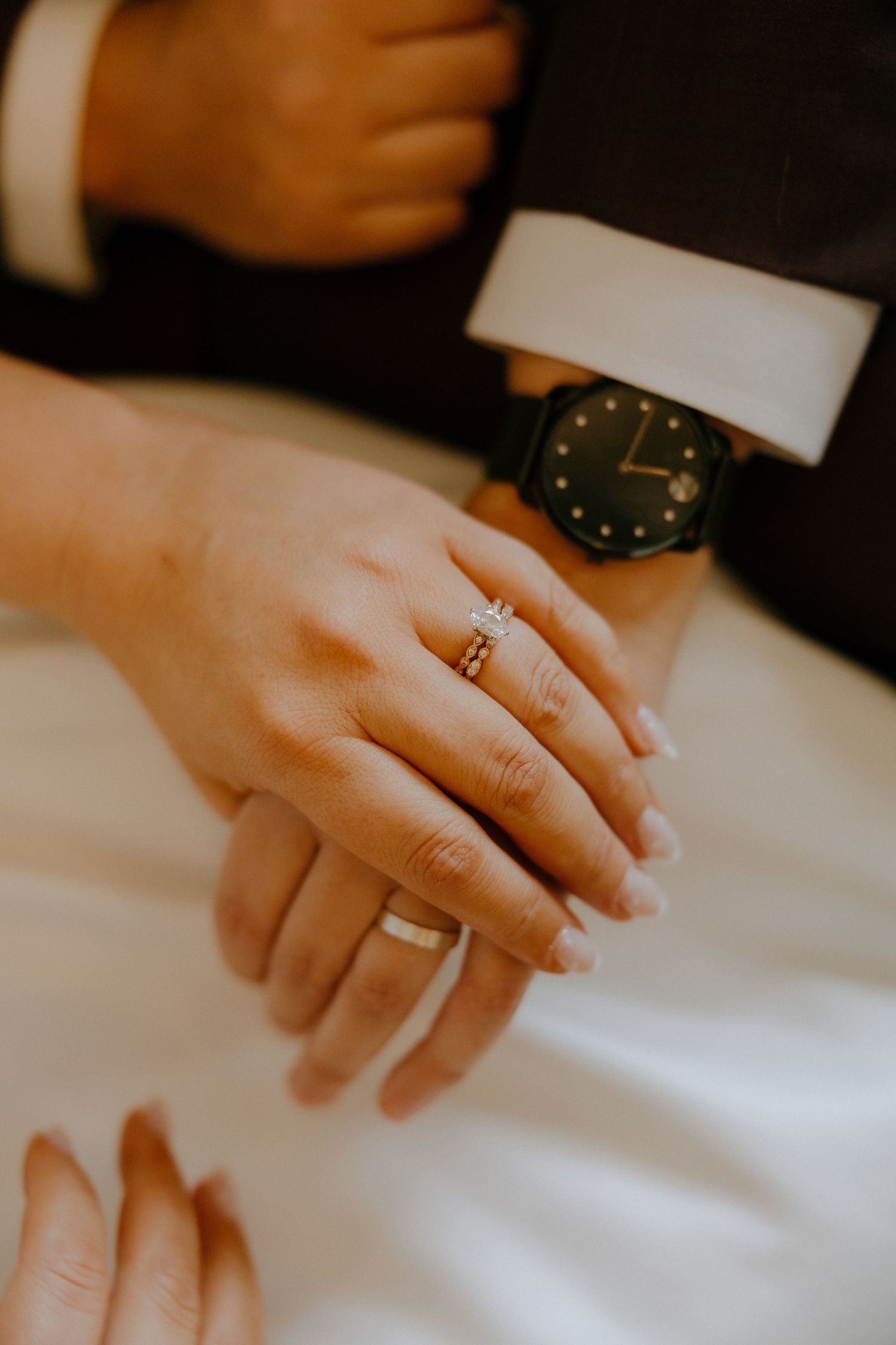 Close-up view of hands wearing engagement and wedding rings on a white tablecloth.