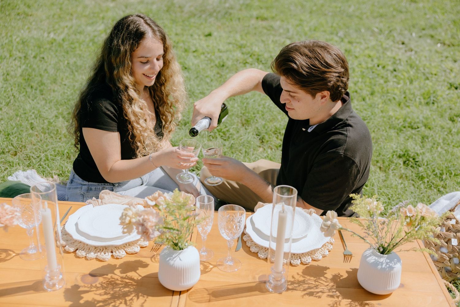Picnic setting with glasses and plates arranged on grass under natural lighting.