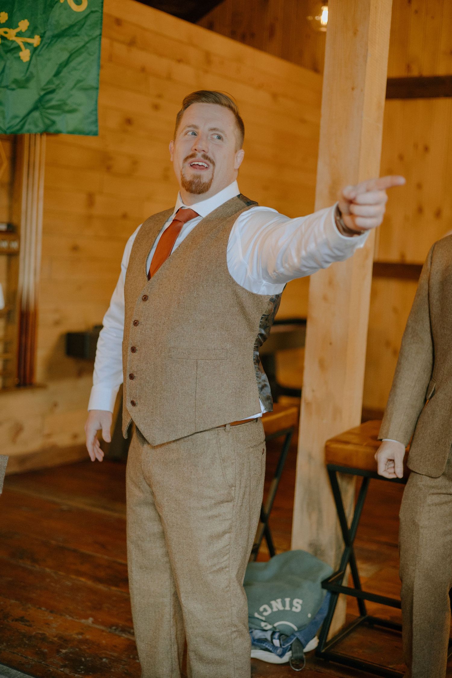 Wedding party members in brown suits and vests share playful moments in a wooden venue.