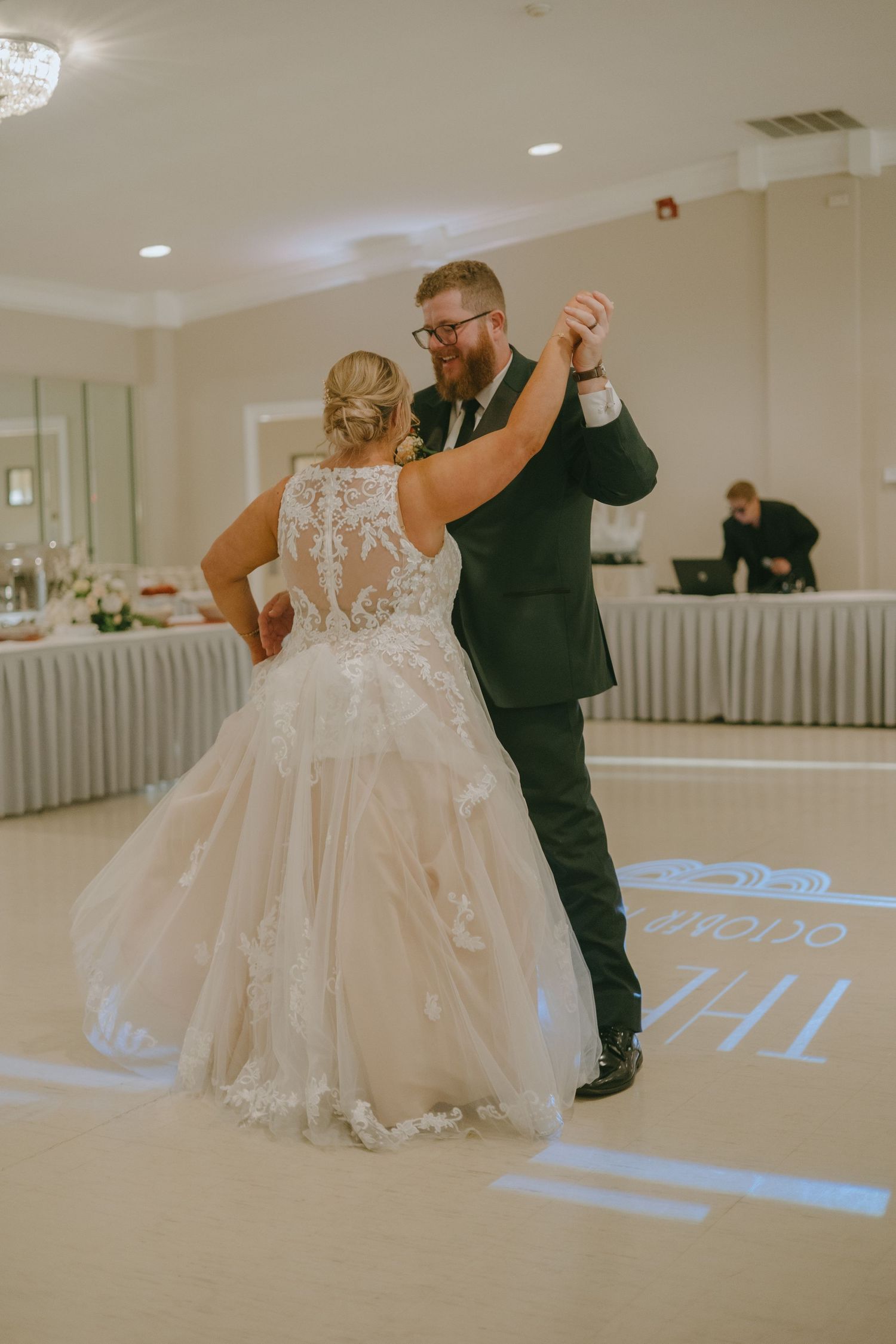 A couple shares their first dance at their wedding reception, with the bride wearing a detailed lace back gown.