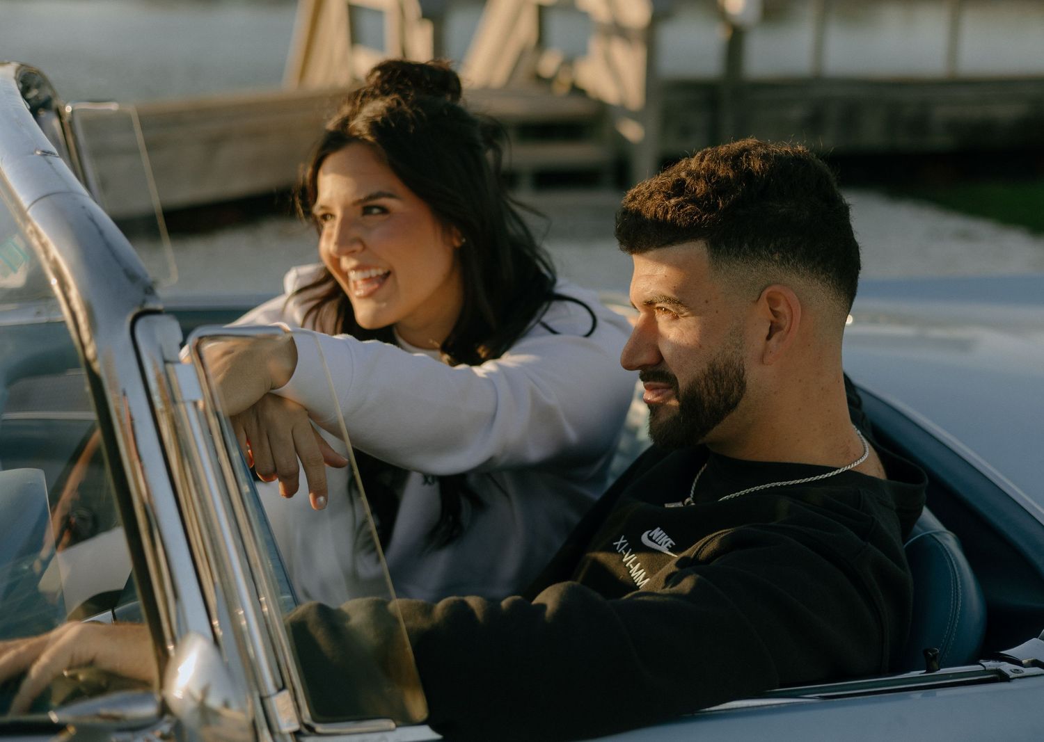 Couple sharing playful moments while sitting in parked car during daytime.