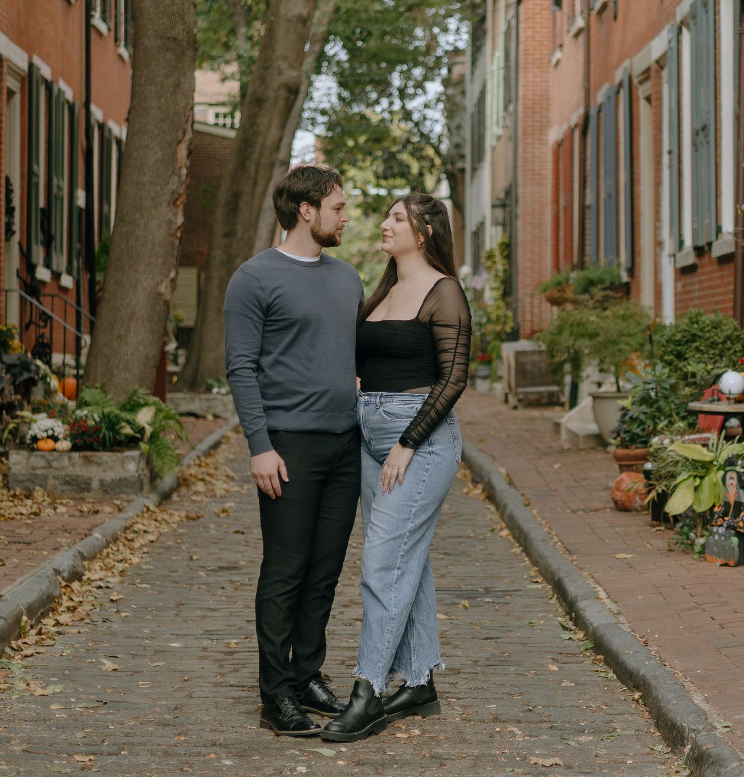 A couple shares a romantic moment on a charming brick-lined street with autumn leaves and historic buildings.
