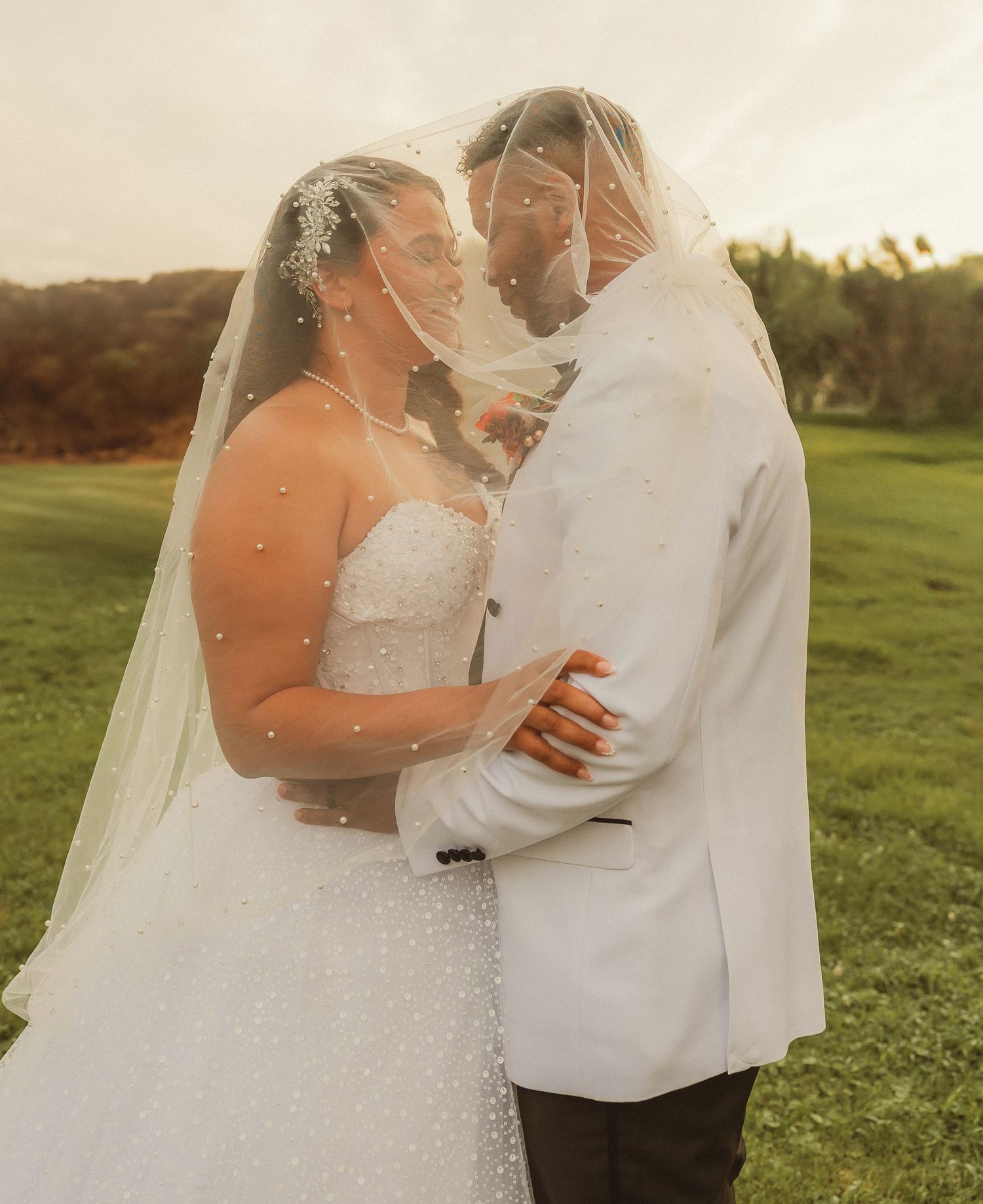 Romantic wedding portraits captured in a sunlit field with flowing veil details.