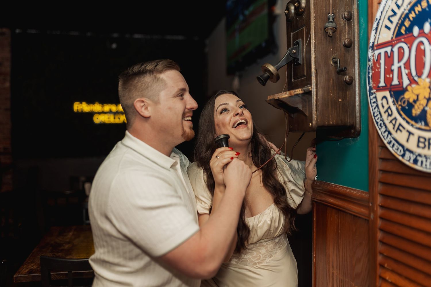 An intimate moment captured in a vintage-style bar with neon signs visible in the background.